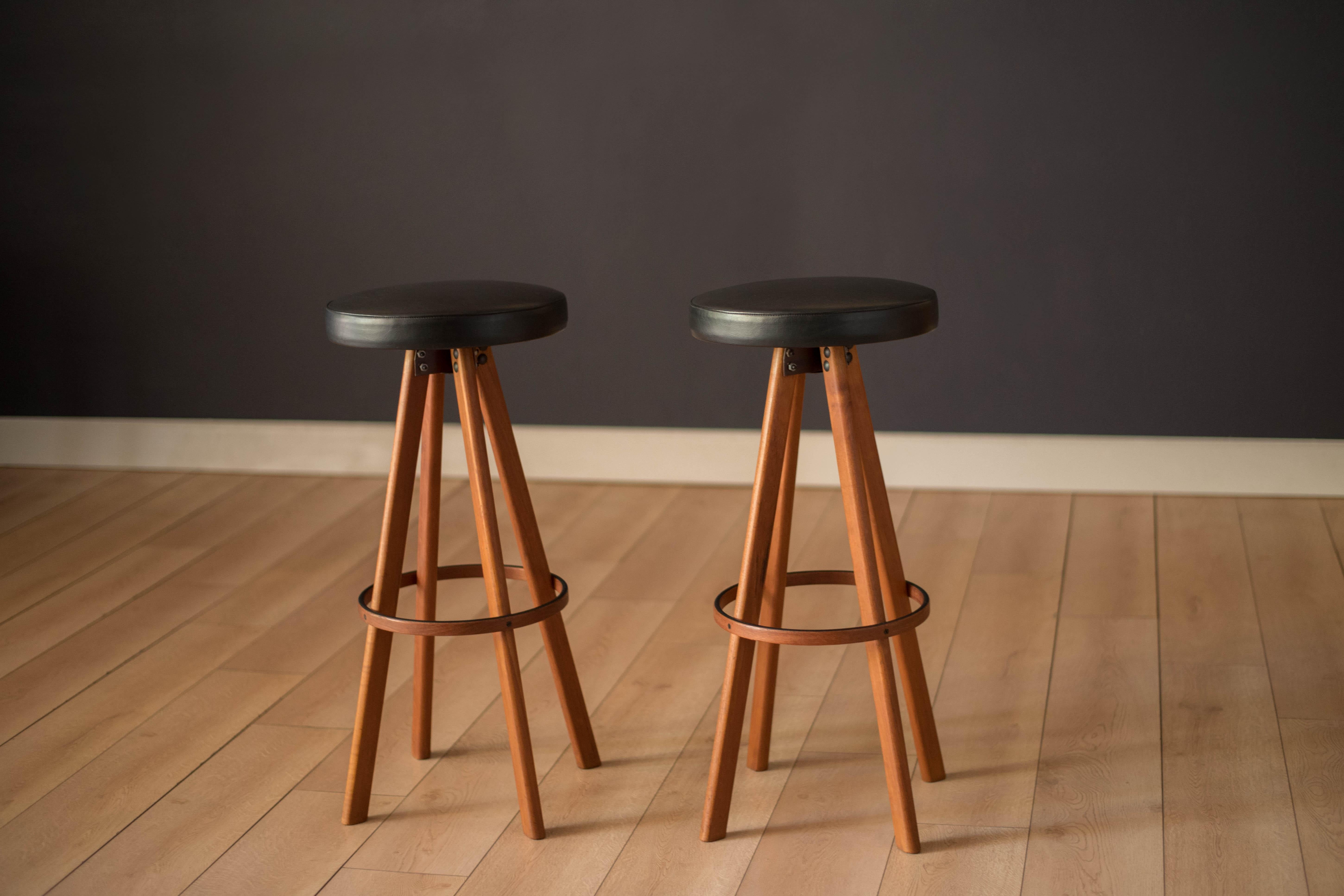 Mid-Century Modern pair of swivel bar stools designed by Hans Olsen for Frem Røjle, Denmark. This set features splayed solid teak legs and round cushion seats in black vinyl. Includes a matching teak footrest with black lacquered detail.