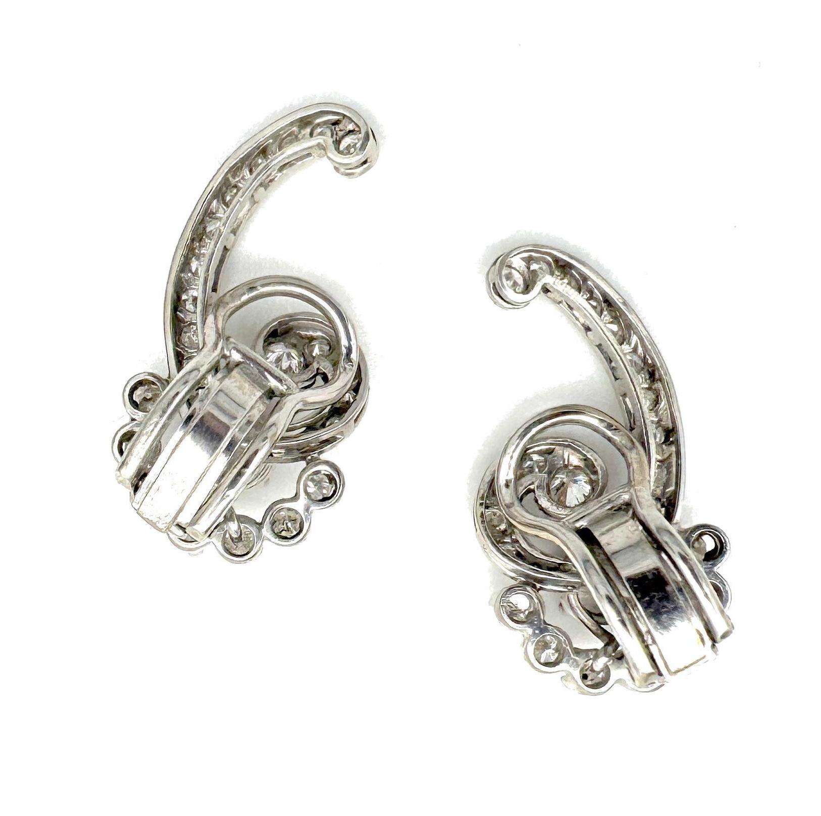 This pair of diamond clip-on earrings was created in the 1950's out of white 14 carat gold. They are designed as large swirls rising out of crescents. The swirls are set with ten graduated diamonds in mille griffe settings leading to a larger
