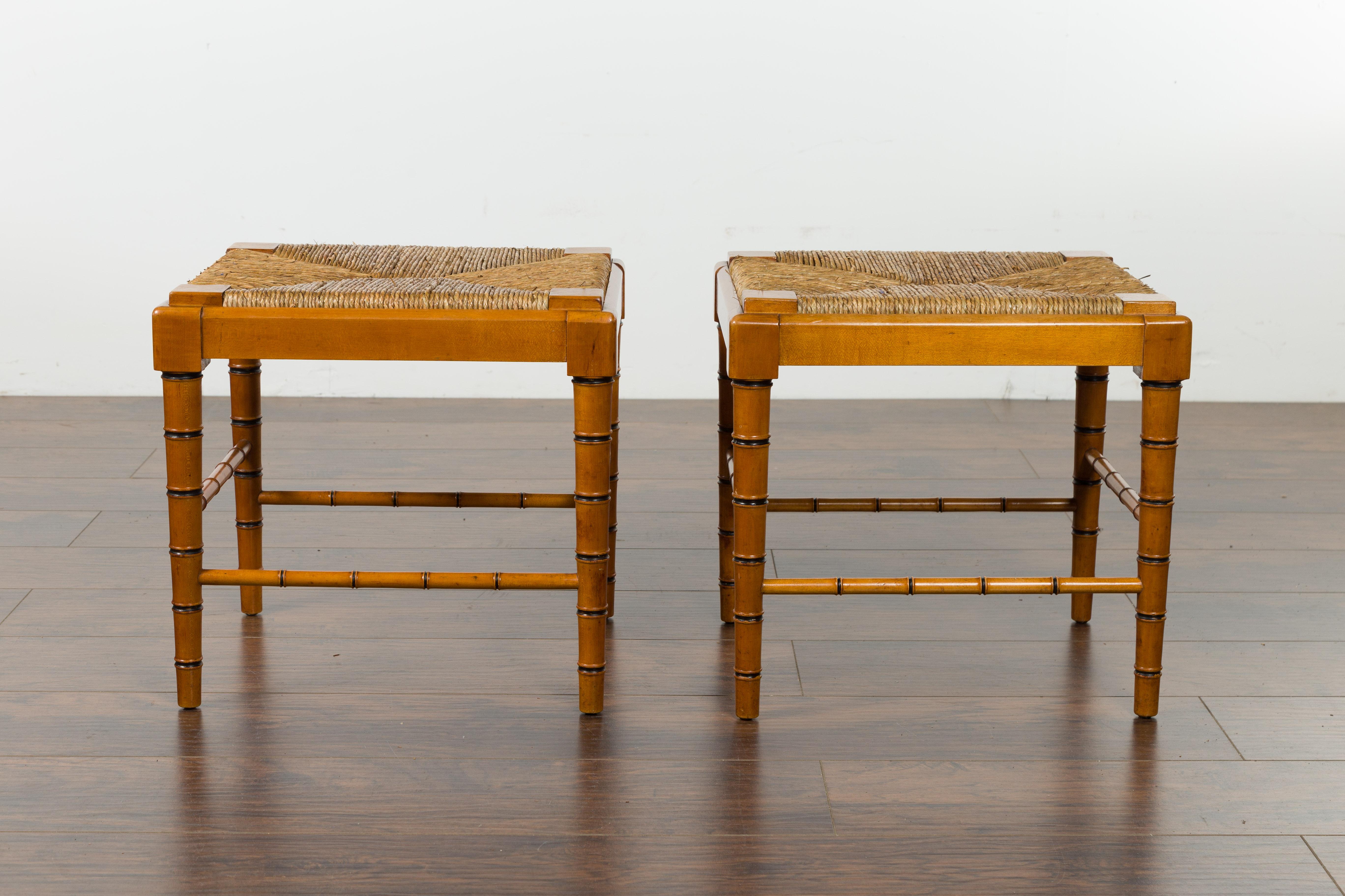 A pair of English vintage walnut stools from the mid-20th century, with faux bamboo bases and rush seats. Created in England during the midcentury period, each of this pair of stools features a rectangular rush seat resting above an elegant faux