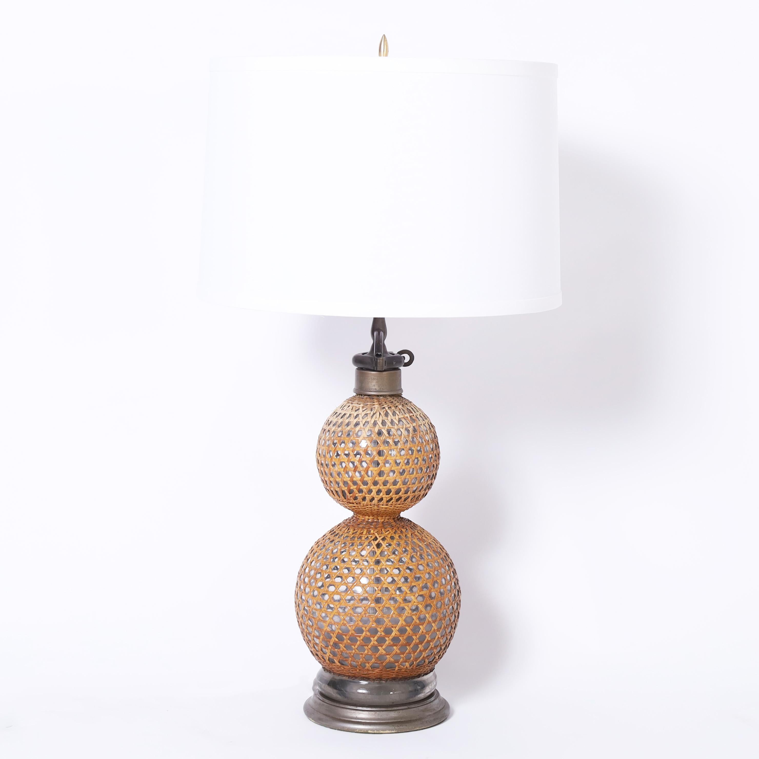 Vintage pair of English table lamps crafted in blown glass in a classic double bulb form wrapped in reed, once seltzer bottles now lamps with pewter hardware. 
