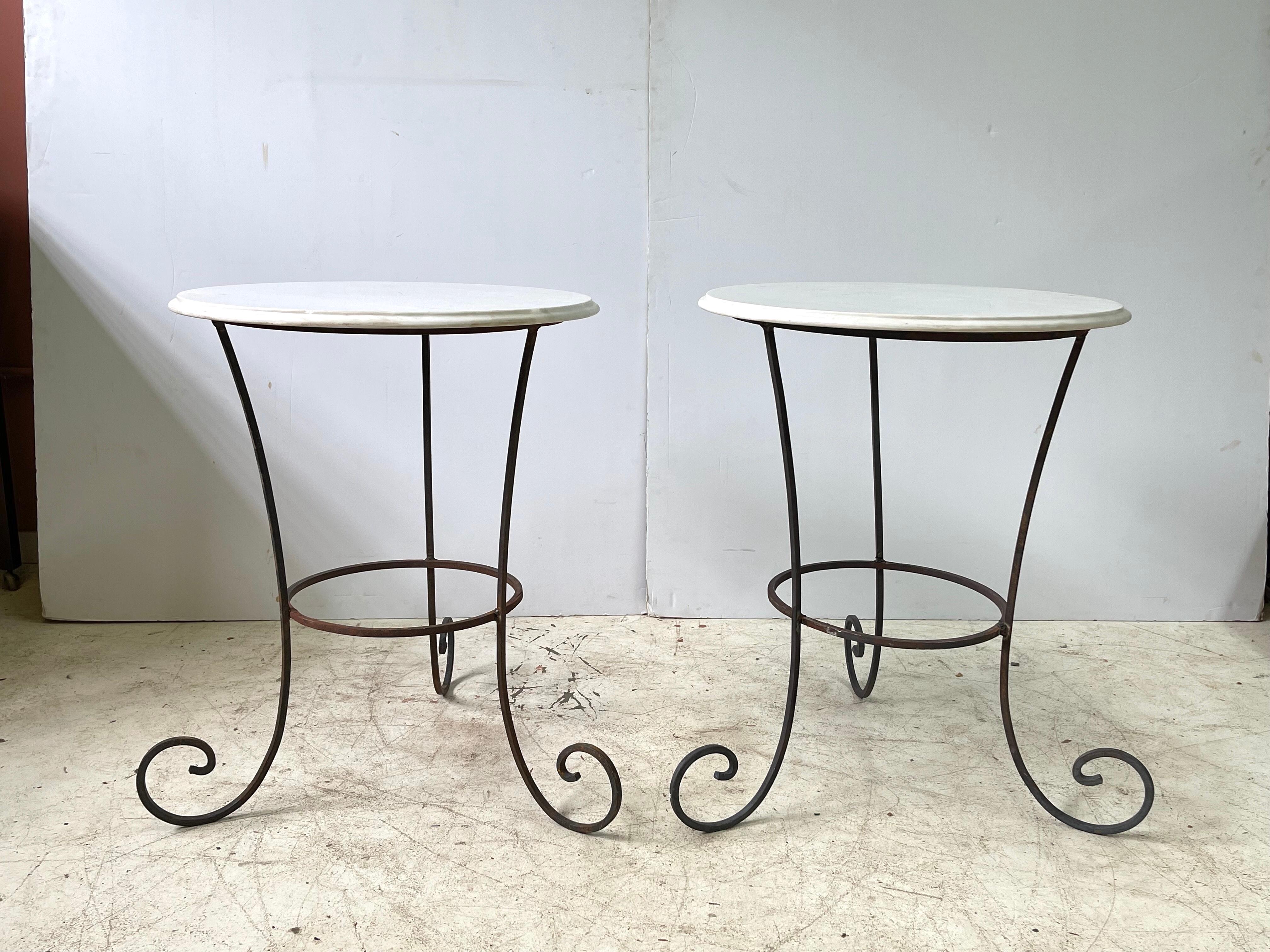 Fabulous pair of 20th Century French scrolling gueridon-style side tables of hand forged iron and having round white marble tops. The table tops each measure 21.5” in diameter, the bases 25” in diameter at the widest point, and their height is