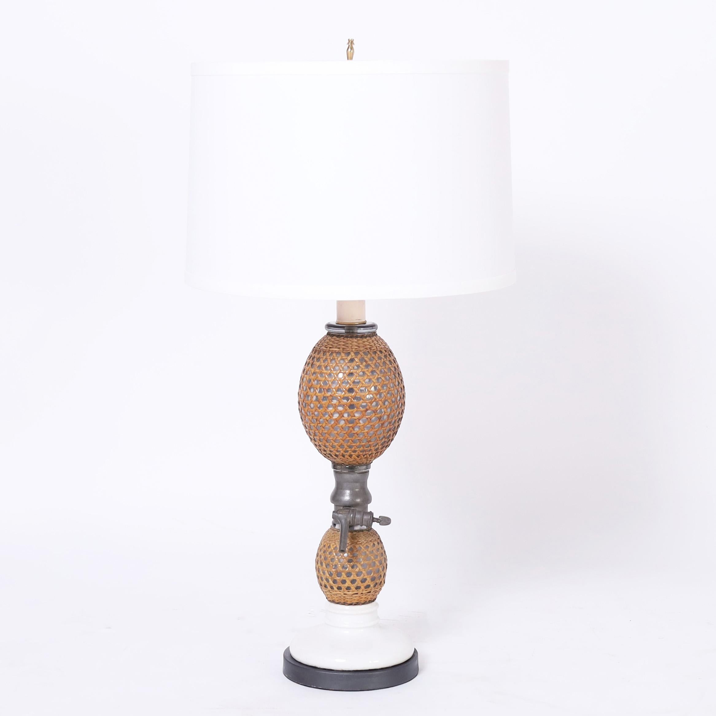 Coppia di lampade da tavolo francesi, un tempo bottiglie di seltz, con due lampadine in vetro soffiato a mano rivestite in rattan intrecciato con ferramenta in peltro e basi in porcellana. 