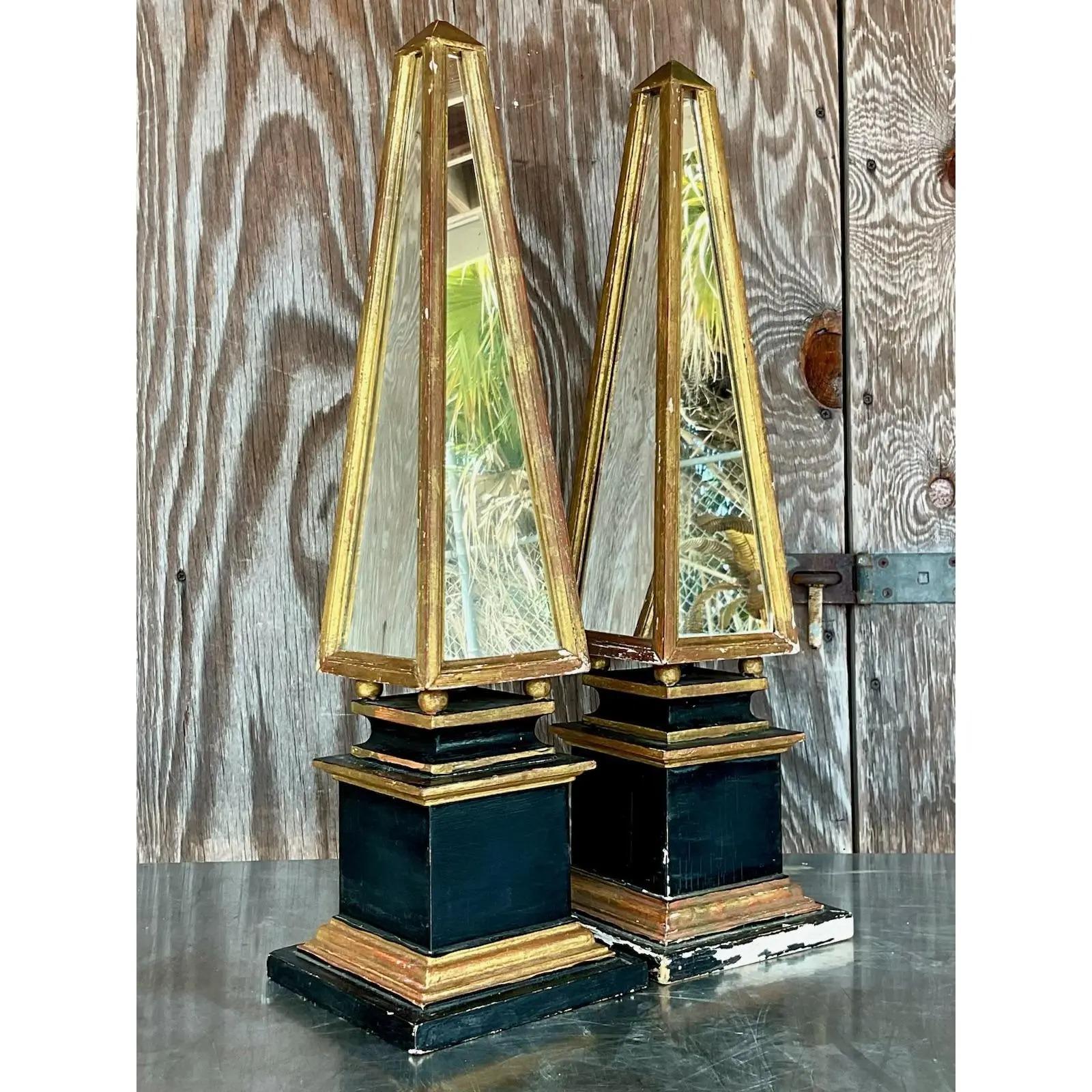 A fabulous pair of vintage giltwood and mirror obelisks in gold and black. Each obelisks is two separate pieces. The top is attached to the bottom. Acquired at a Palm Beach estate.