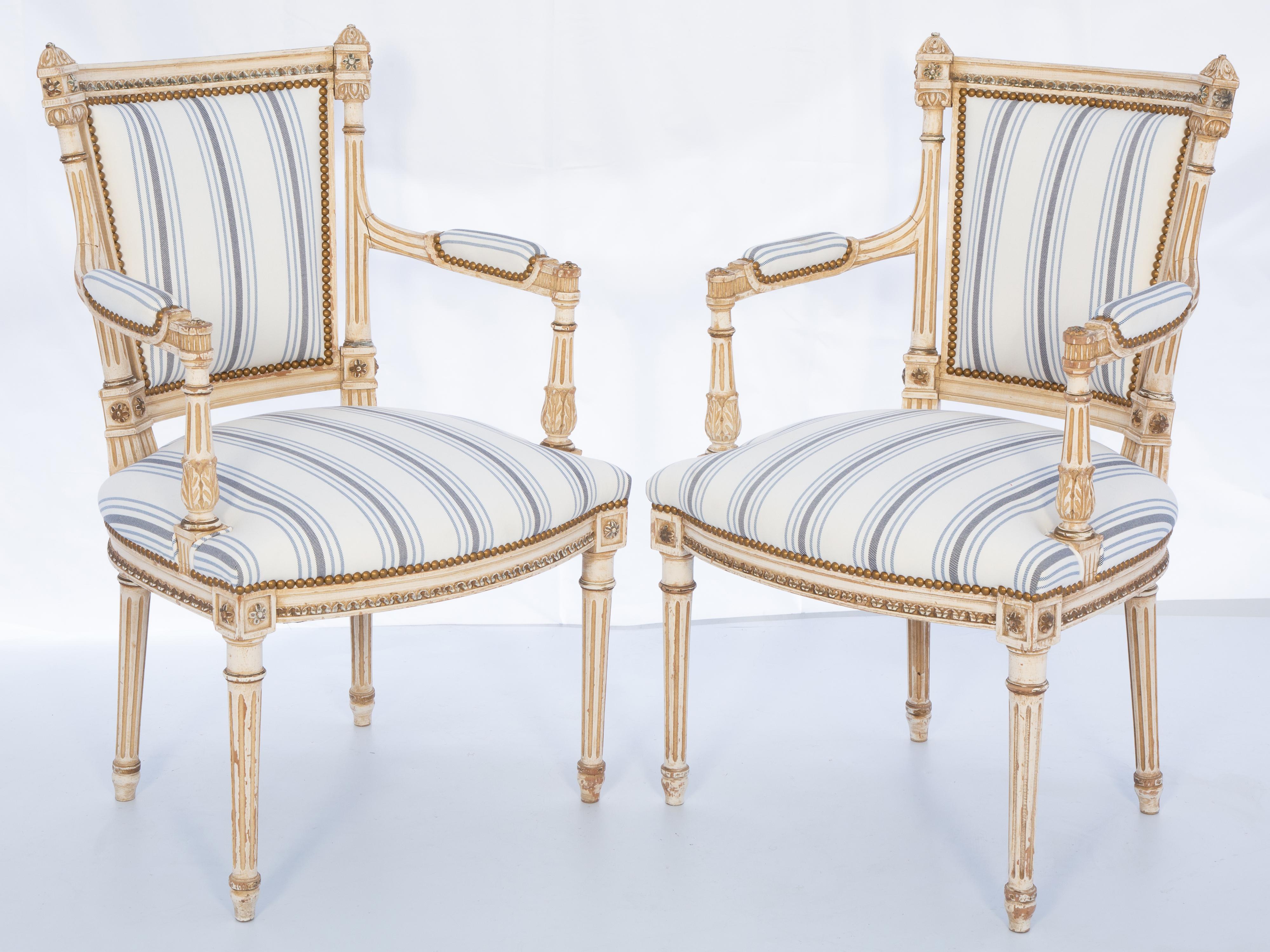 Paire de fauteuils, dont la finition peinte présente une usure naturelle. Sa traverse quadrillée, flanquée de fleurons à cassolette, repose sur des montants ronds et cannelés qui se prolongent par des accoudoirs aux coudes paddés et reposent sur des
