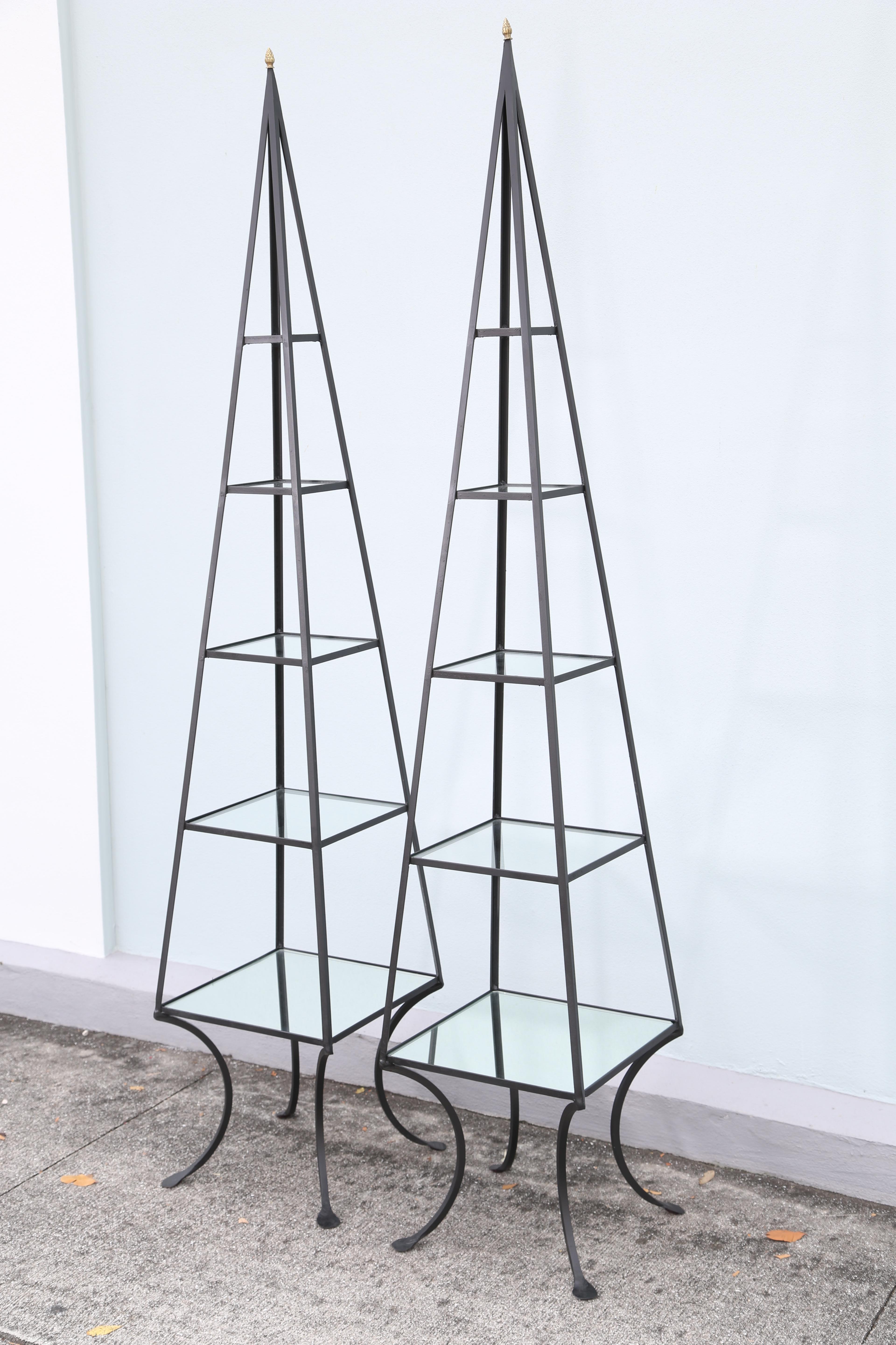 Pair of wrought iron obelisk étagères with five display shelves.
Brass acorn finial on top and lily pad feet.