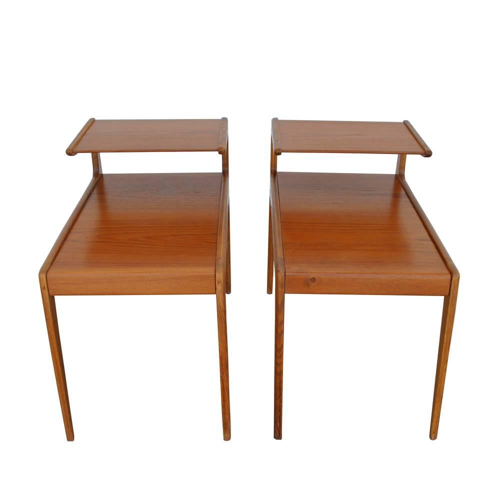 A pair of vintage Scandinavian end tables by Kurt Ostervig. Features two-tiered design and a continuation of the back legs of the tables, giving the tables a seamless quality to their design. With the prominent angles and surfaces of Scandinavian