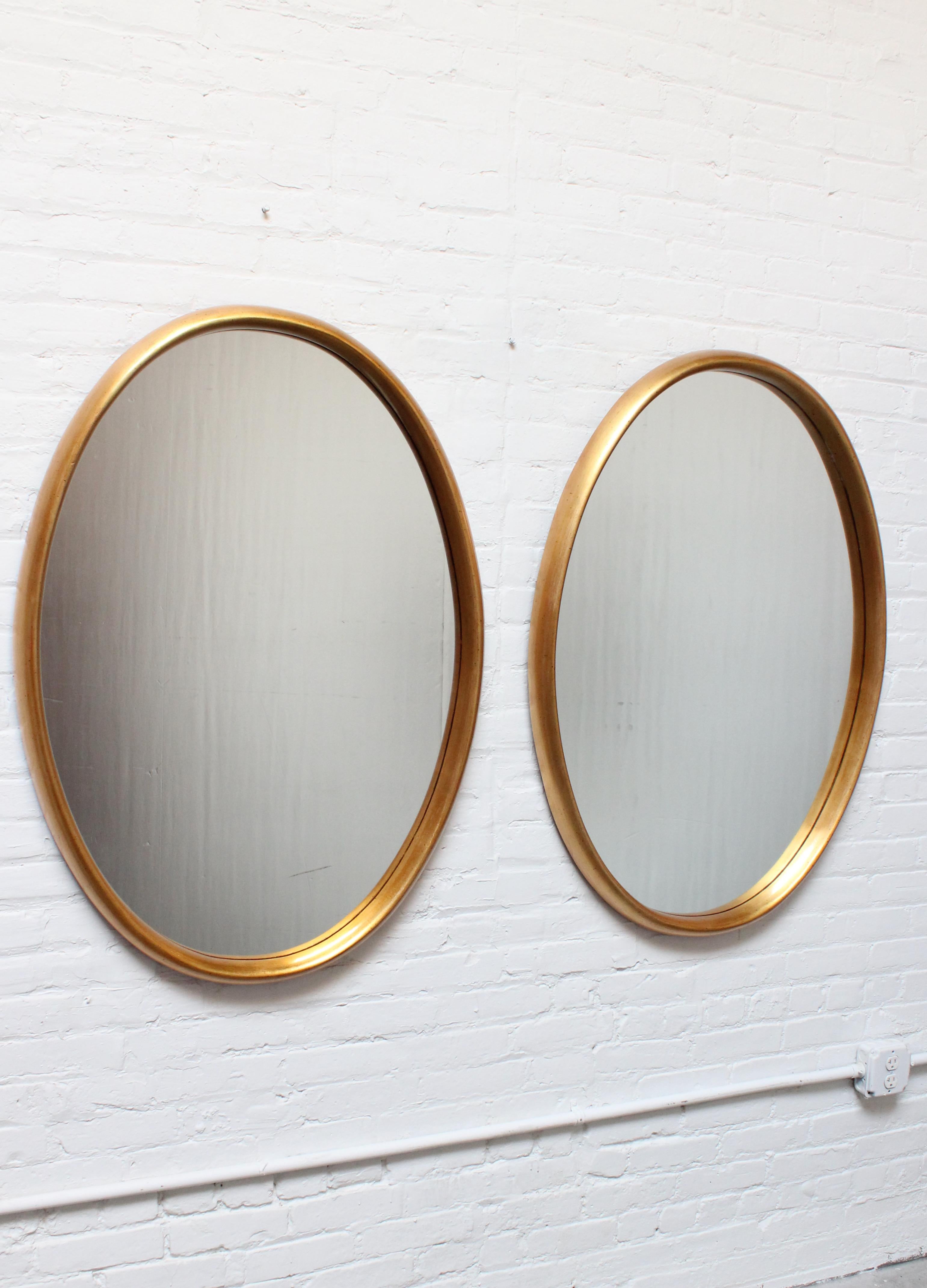Pair of wide, oval-form Labarge mirrors composed of inset glass within deep, gold leaf frames. There is minor wear to the glass (most notably, a light, long scuff to the right mirror's glass, as shown in the last image). Does not affect the clarity