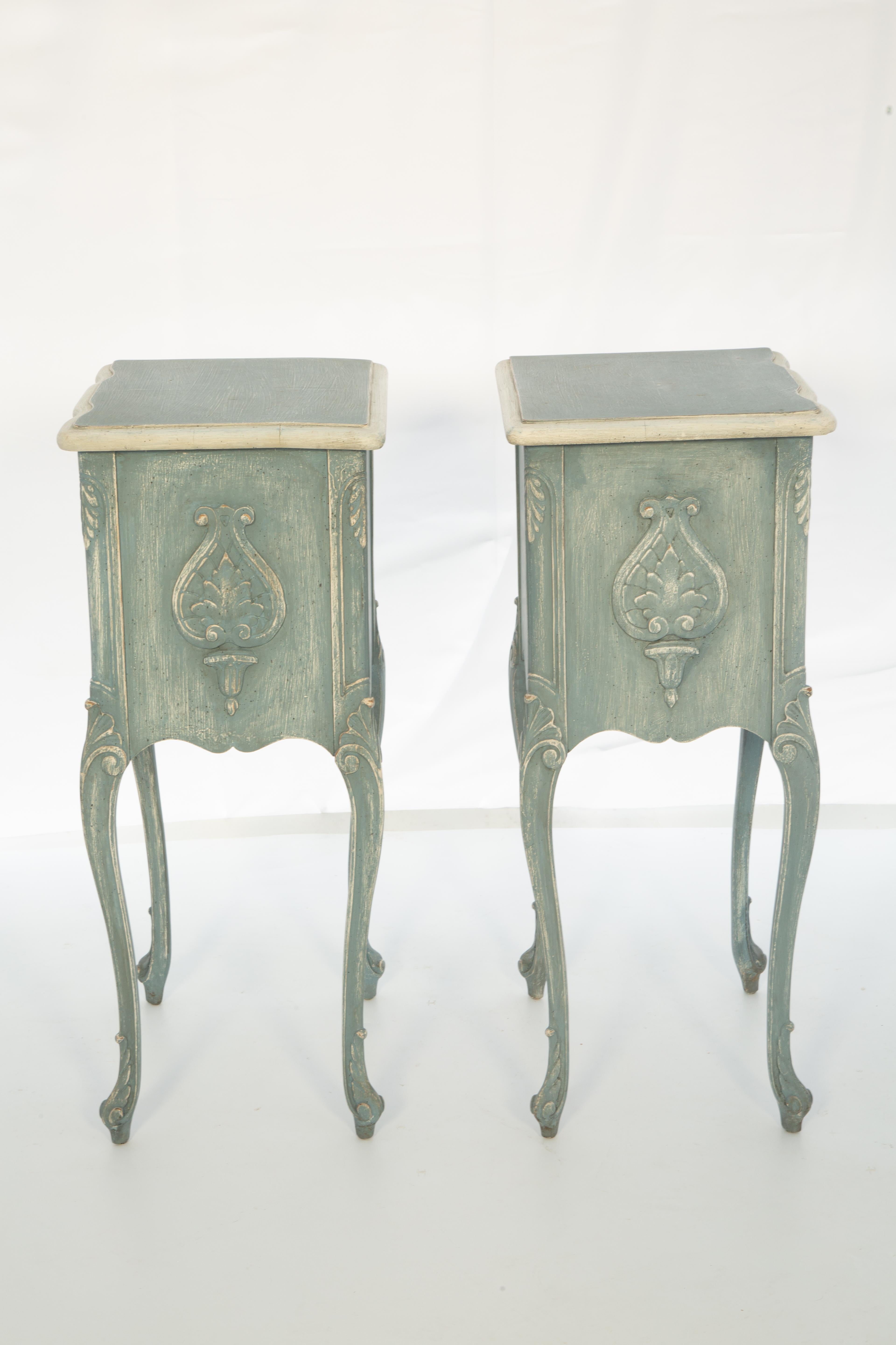 Pair of petite bedside chests, having a painted finish showing desirable wear. Each nightstand having a rectangular molded top, on a case with double stacked drawers, each carved with horns and scrollwork, centered with a cartouche. It's shaped