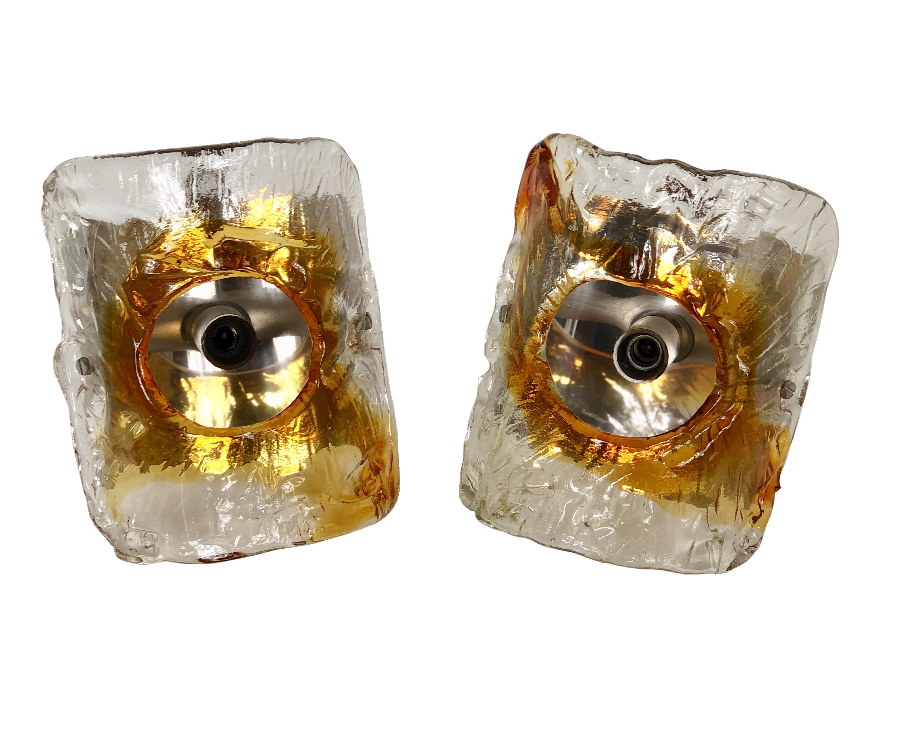A pair of Italian wall sconces by Mazzega, produced, circa 1970s, each with convex shades in textured clear and amber Murano glass, surrounding a single exposed socket, affixed to a chrome backplate.