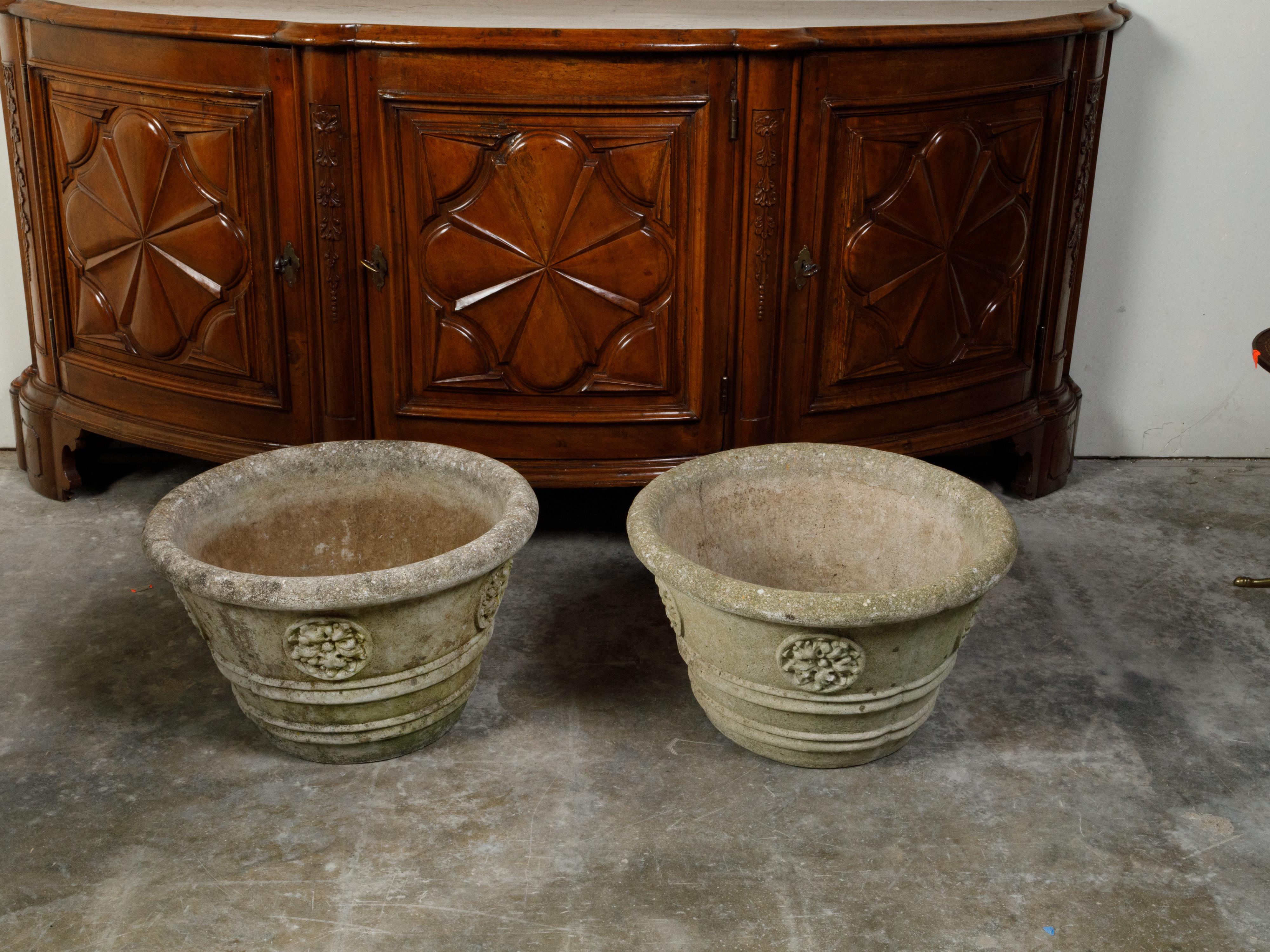 A pair of vintage cast stone planters from the mid 20th century, with rosette motifs. We have two pairs available, priced and sold $3,750 per pair. Created during the Midcentury period, each of this pair of planters features a circular tapering cast