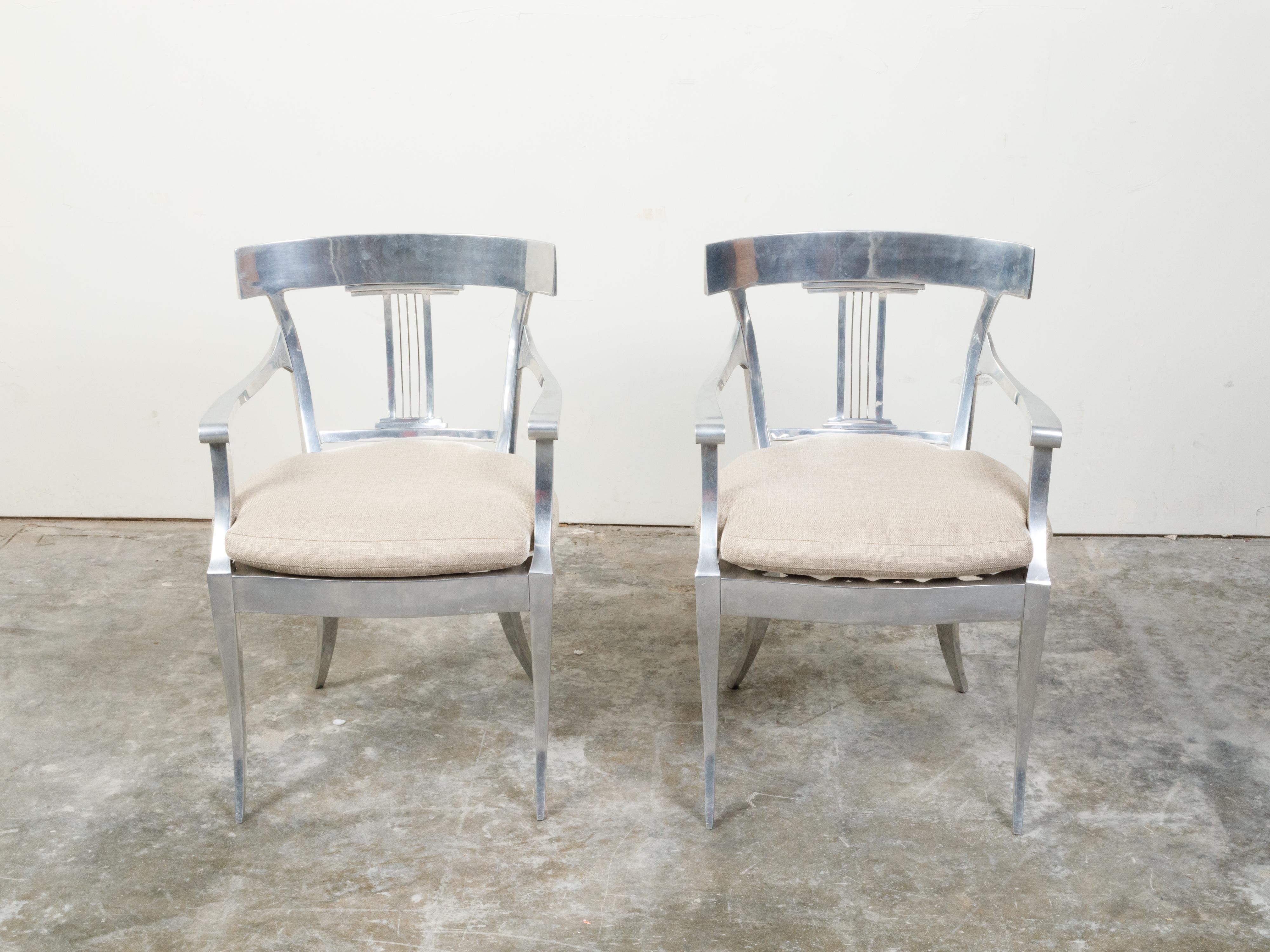 A pair of vintage steel armchairs from the mid-20th century, with curving backs, pierced splats and custom cushions. Created during the mid-century period, each of this pair of steel armchairs features an in-curving back adorned with a pierced