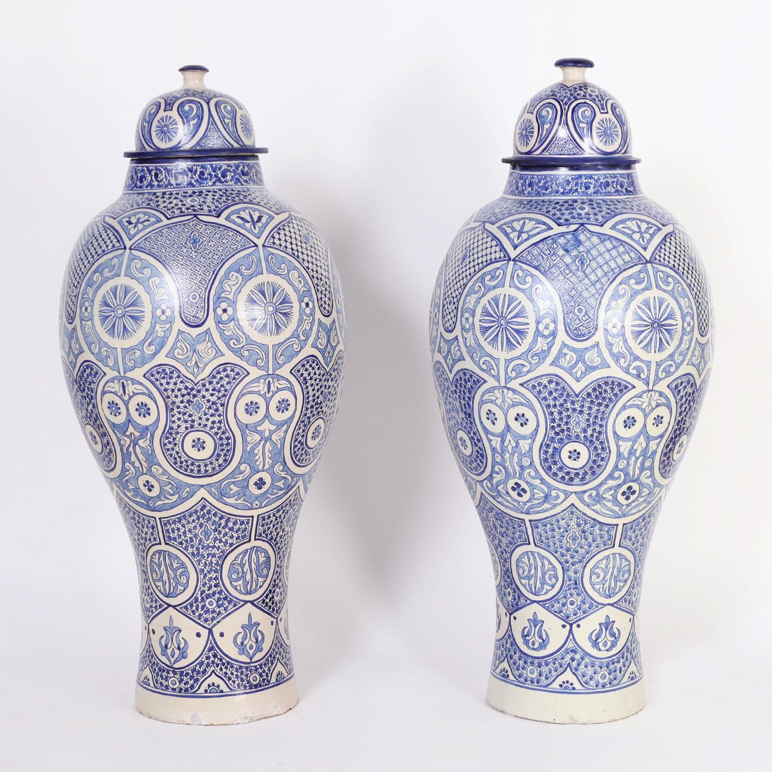 Impressive pair of vintage Moroccan palace size lidded urns crafted in terra cotta in classic form with distinctive hand decorated Mediterranean designs in alluring blue tones. 