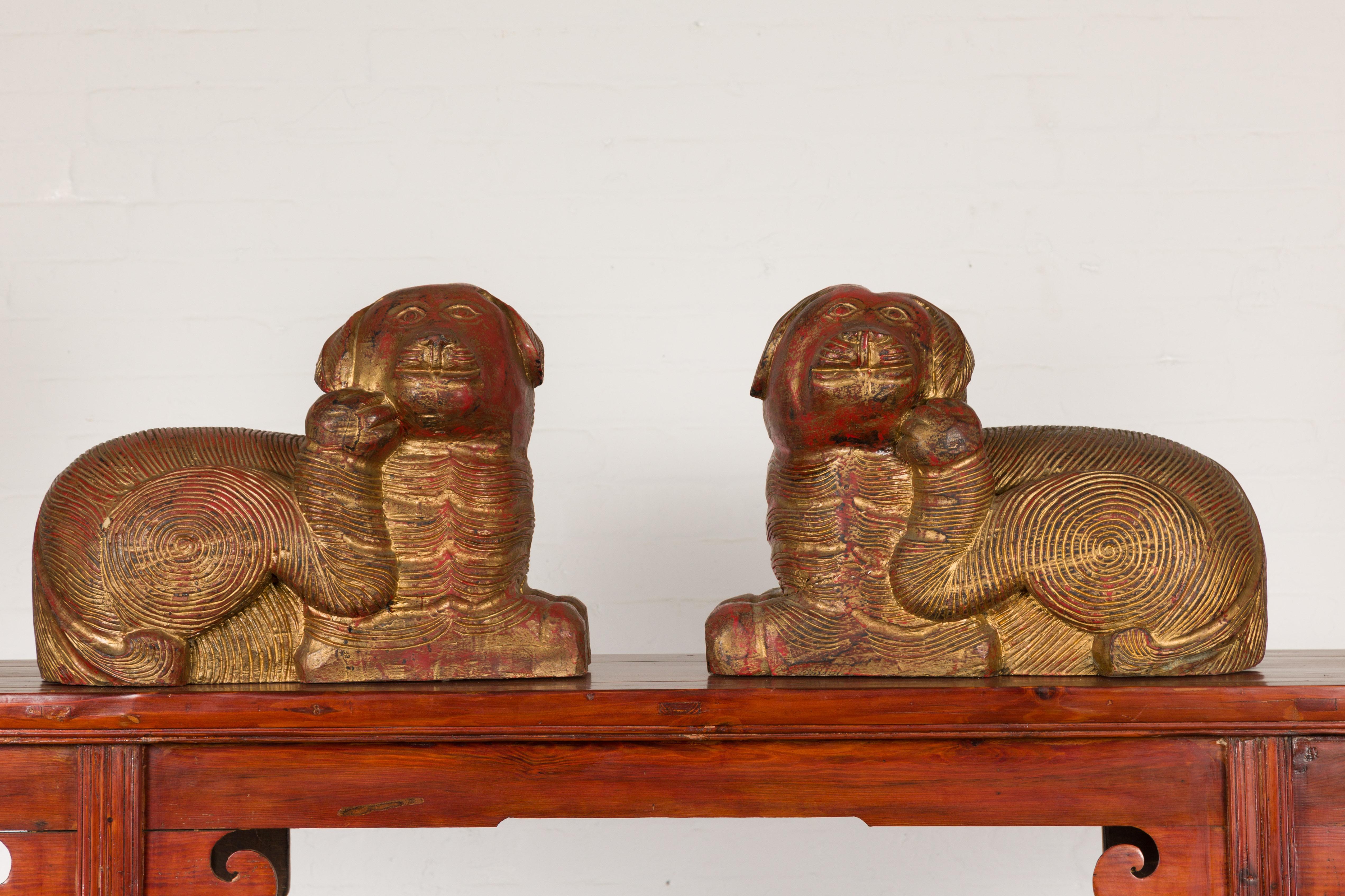 Ein Paar thailändische, geschnitzte, hängende Fabelwesen aus der Mitte des 20. Jahrhunderts mit vergoldeter Oberfläche und rotem Unterton. Entfesseln Sie den Charme der Mythen mit diesem exquisiten Paar geschnitzter thailändischer Holzfiguren aus