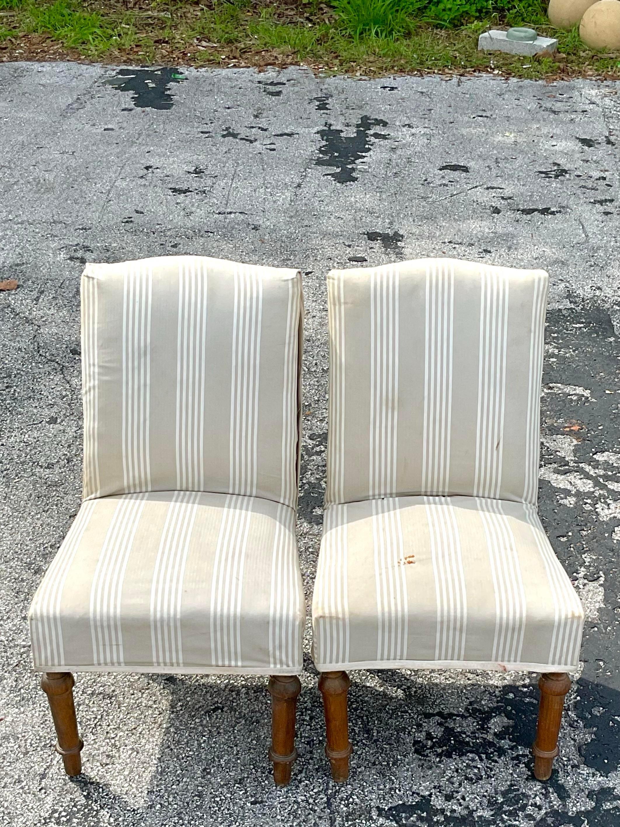 Incredible pair of old American slipper chairs with original carved wooden legs and antique style upholstery application. The chairs have all the markings of old traditional furniture construction with visible nails on the upholstery making them