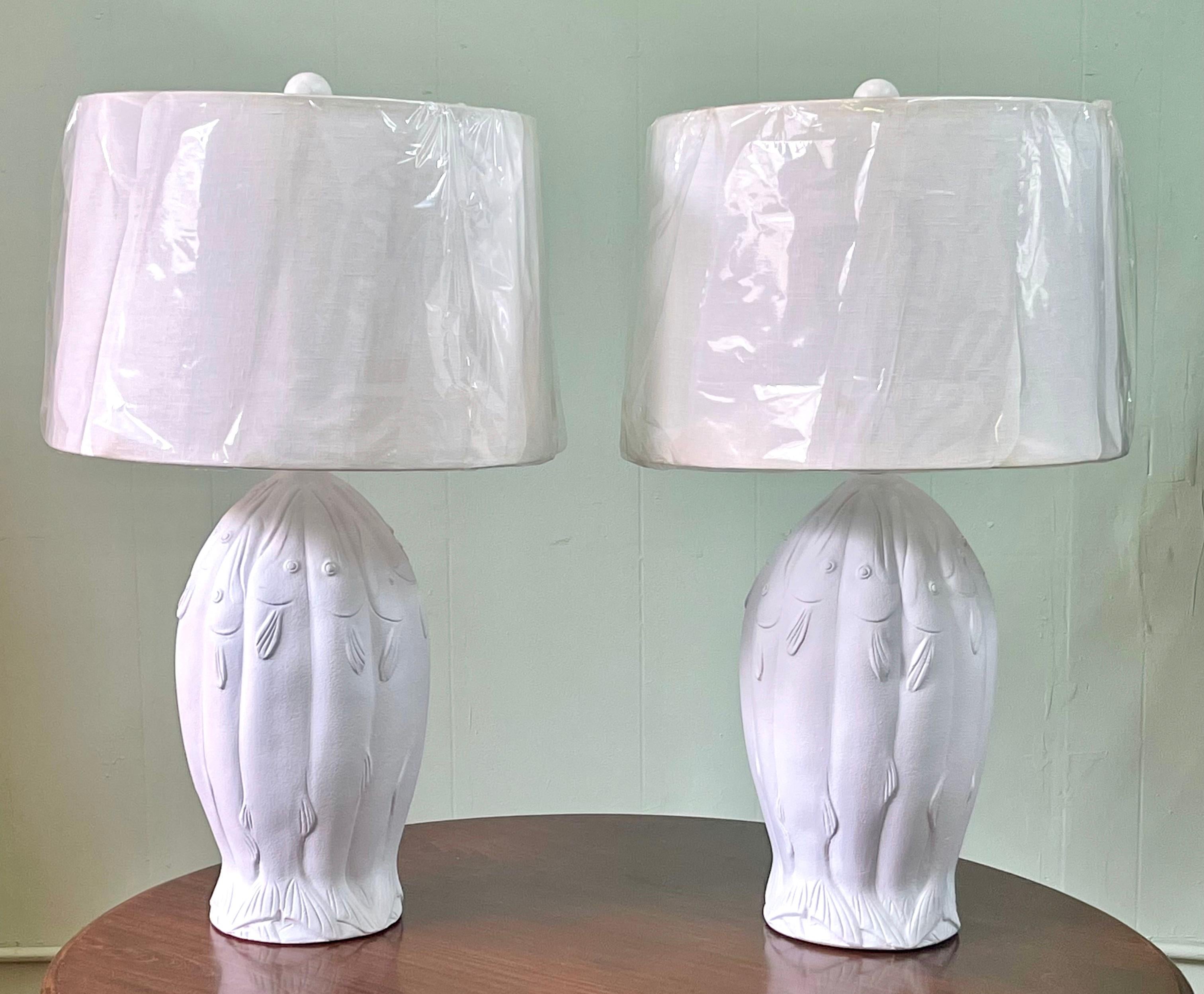 Pair of 20th Century plaster lamps in white with a design of stylized fish cast in relief and forming the shape of an urn. Lamps are signed CL.

The measurement to the top of the finial is 31.5