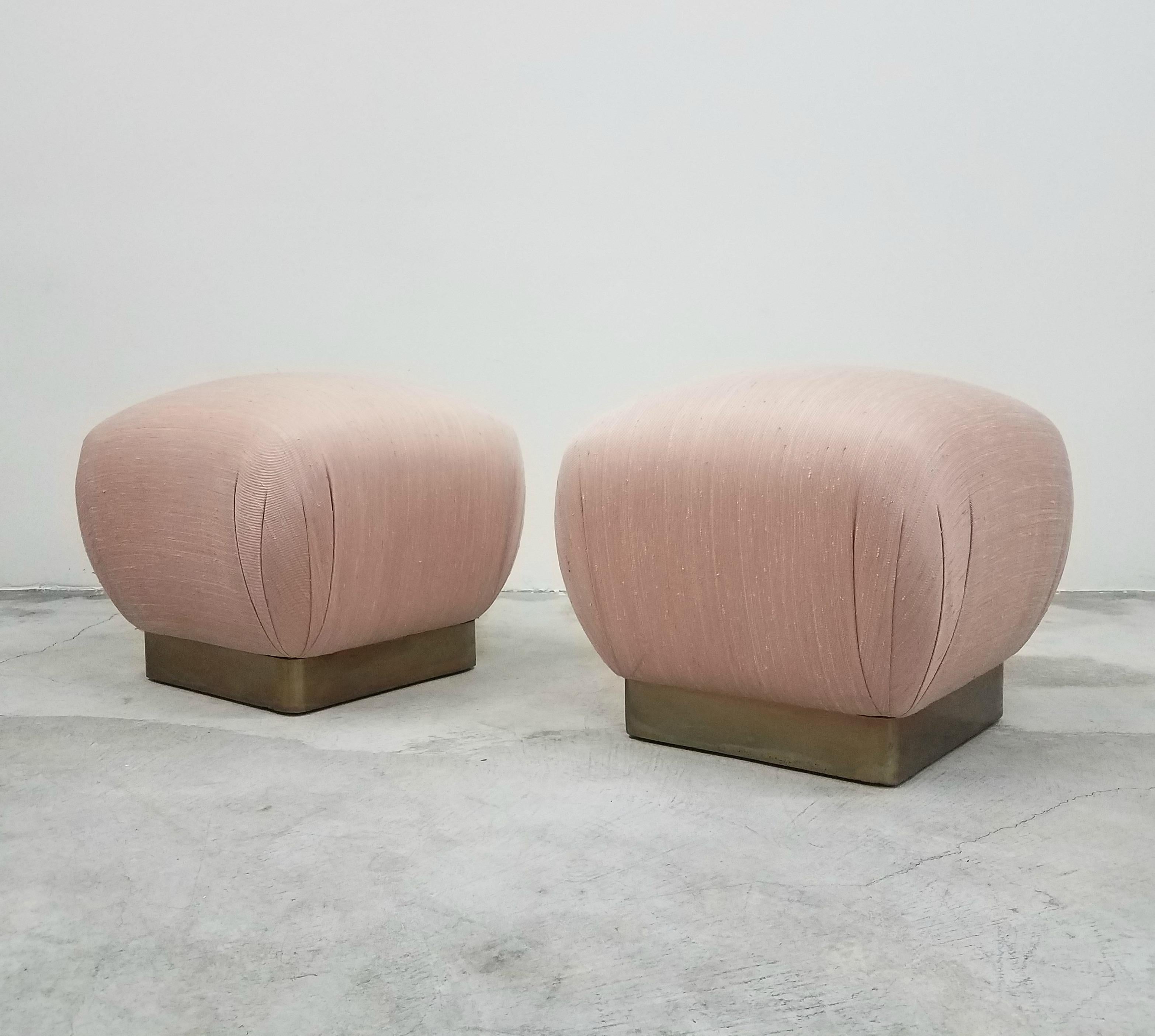 Gorgeous pair of Regency Style pouf ottomans. Pair has beautifully patinated original brass plinth bases. Great for added seating or decor. 

Original blush pink upholstery is in good, usable condition. Professional reupholstery available.
