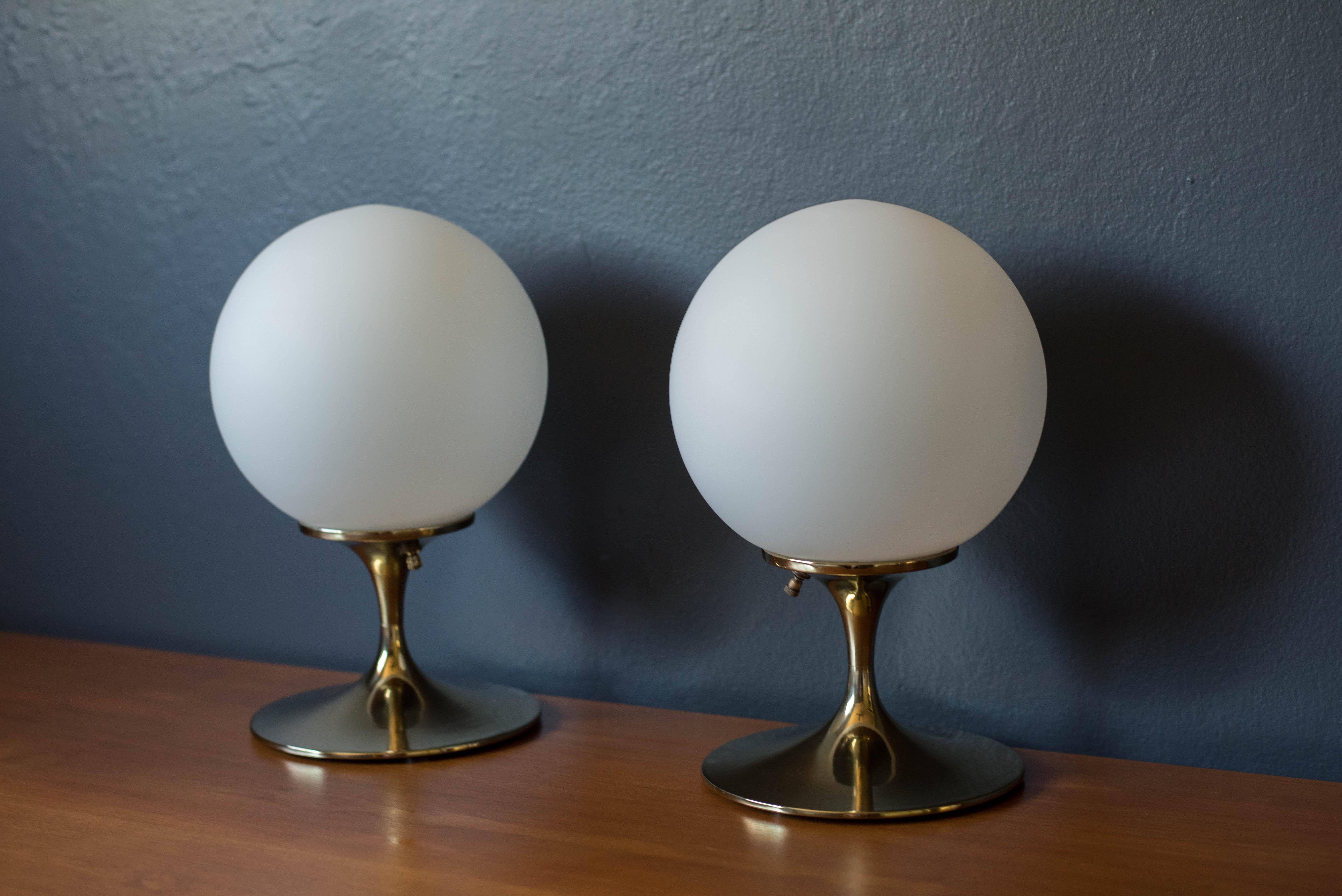 Mid century modern pair of accent table lamps in brass manufactured by Laurel Lamp Co. This set features a sculptural tulip base and illuminating white frosted glass globe shades. Price is for the pair.