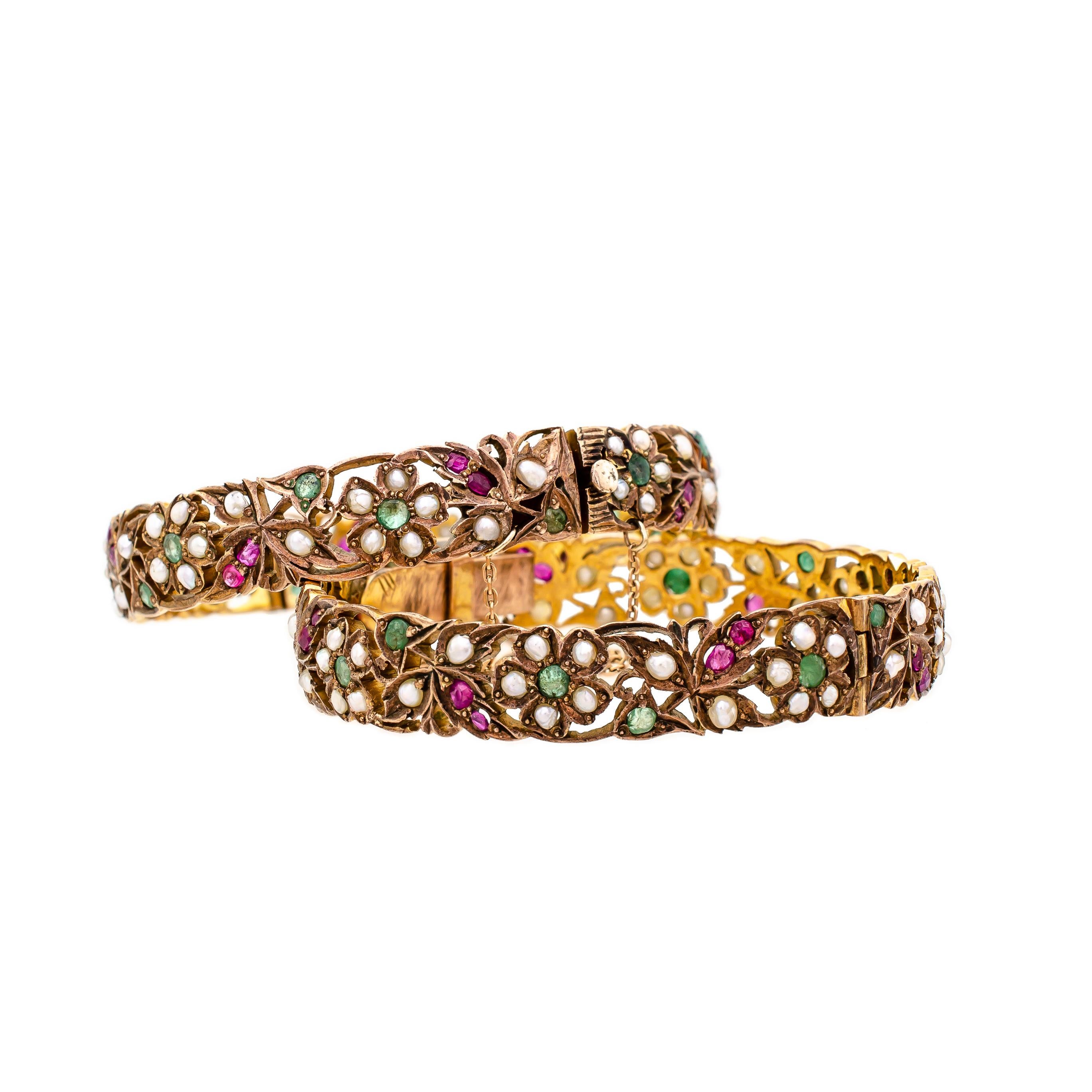 Exquisite, stylish vintage pair of silver-gilt and gem-set bangle bracelets from India. Each hinged set with beautiful emeralds, lovely rubies, and elegant seed pearls. Both bangles have hidden clasps and gold safety chains. These handcrafted