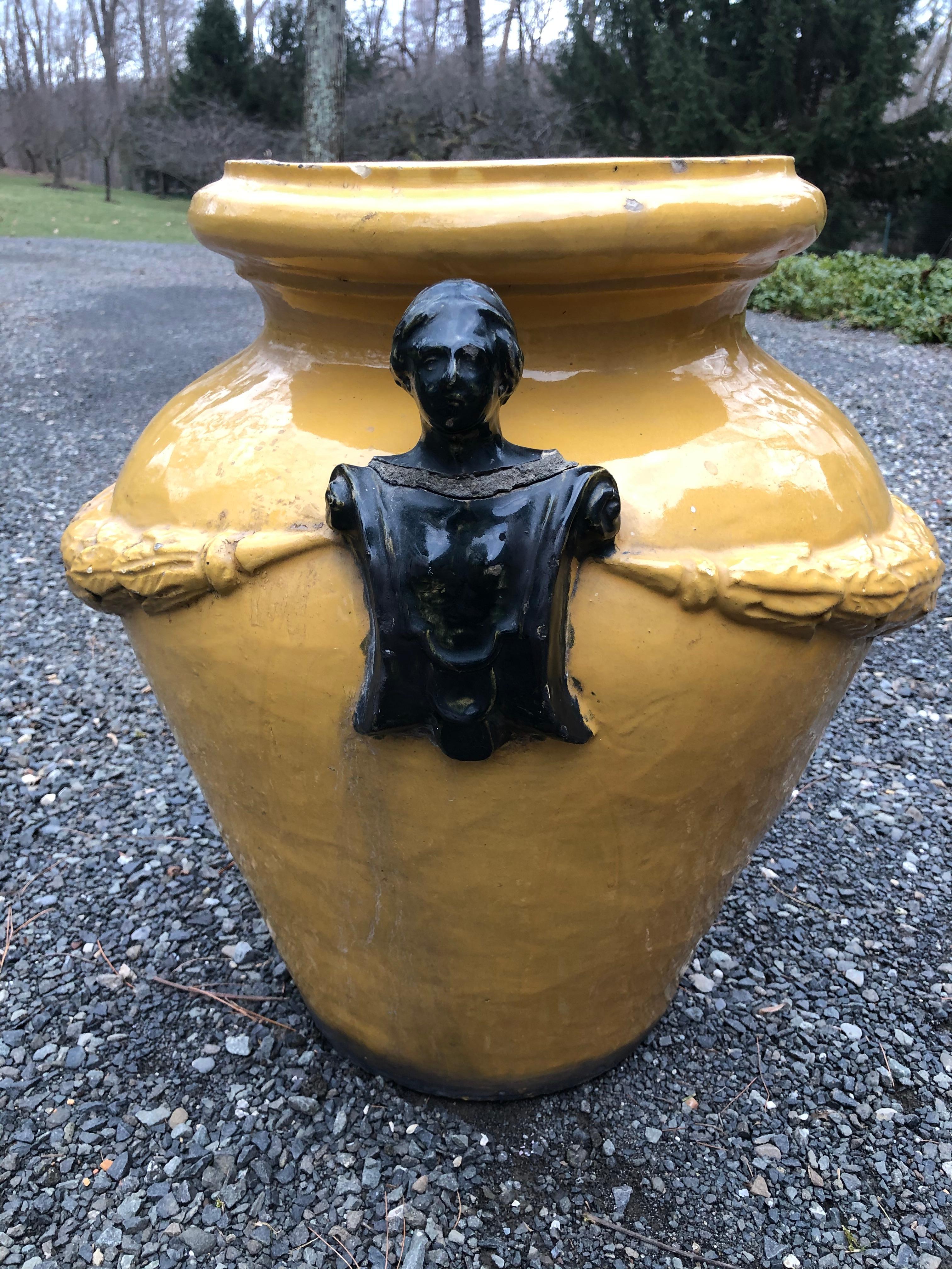 A fabulous pair of substantial jardinières from Italy. Glazed in a great shade of saffron, the jardinières are made of terracotta. Each has a raised swag of leaves surrounding it. The handles depict the torso of a decorated gentleman. These