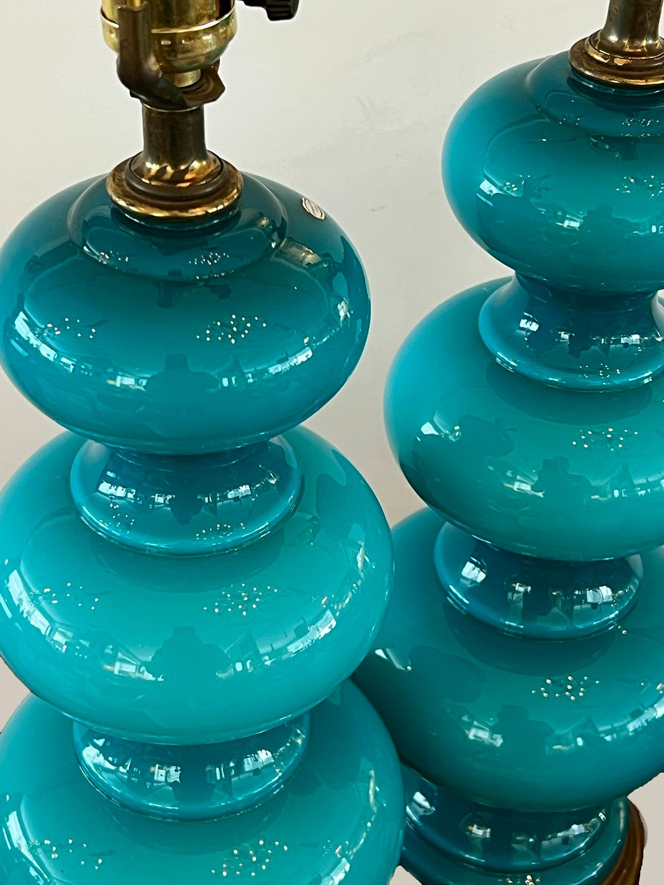 the French made cased-glass bodies of graduated triple-gourd form resting on brass bases; in a deep teal color accentuated by the cased-glass process of fusing together multiple layers of glass; each with foil label 'BASE MADE IN FRANCE'; height: