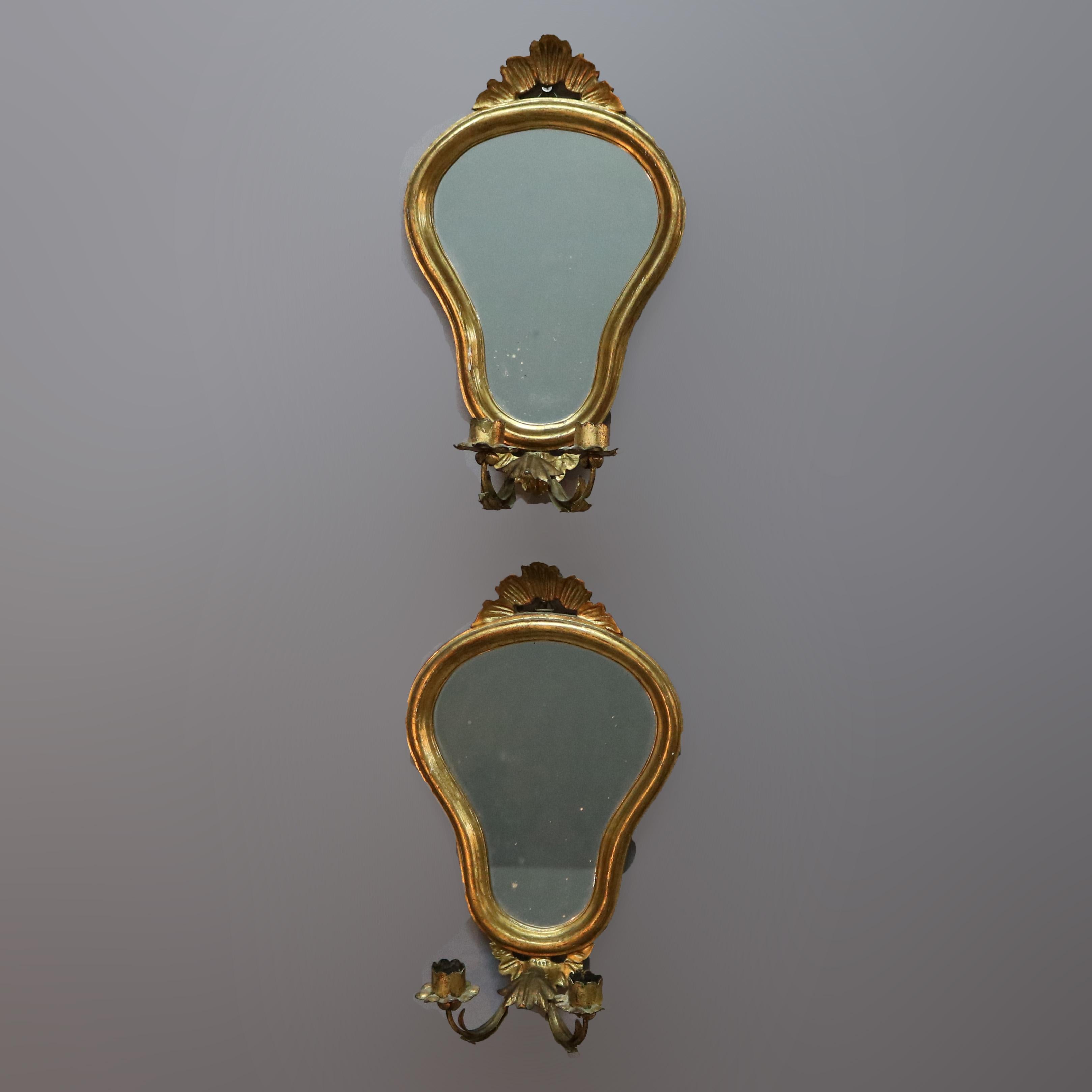 A pair of vintage Venetian wall sconces offer giltwood frames in shield form with carved foliate cresta surmounting shaped mirror with two C-scroll foliate arms terminating in candle sockets, 20th century.

Measures: 15.5