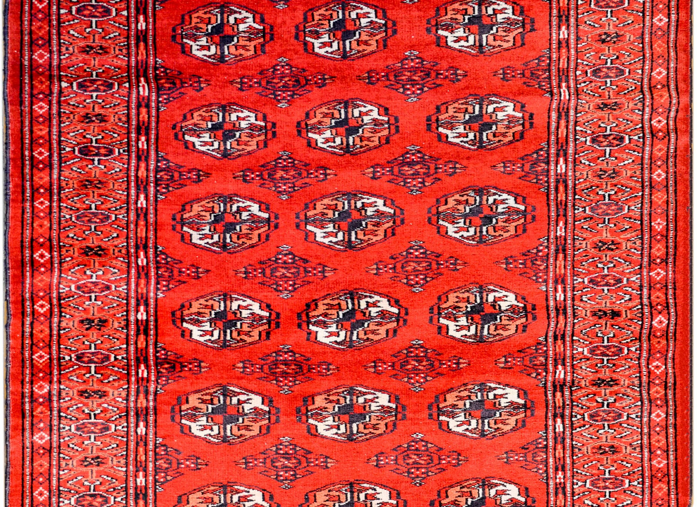 An amazing vintage Pakistani Bokhara rug with an all-over pattern of crimson, indigo, and white wool lozenge form medallions on a dark crimson background. The border is wide with a large complementary geometric pattern.