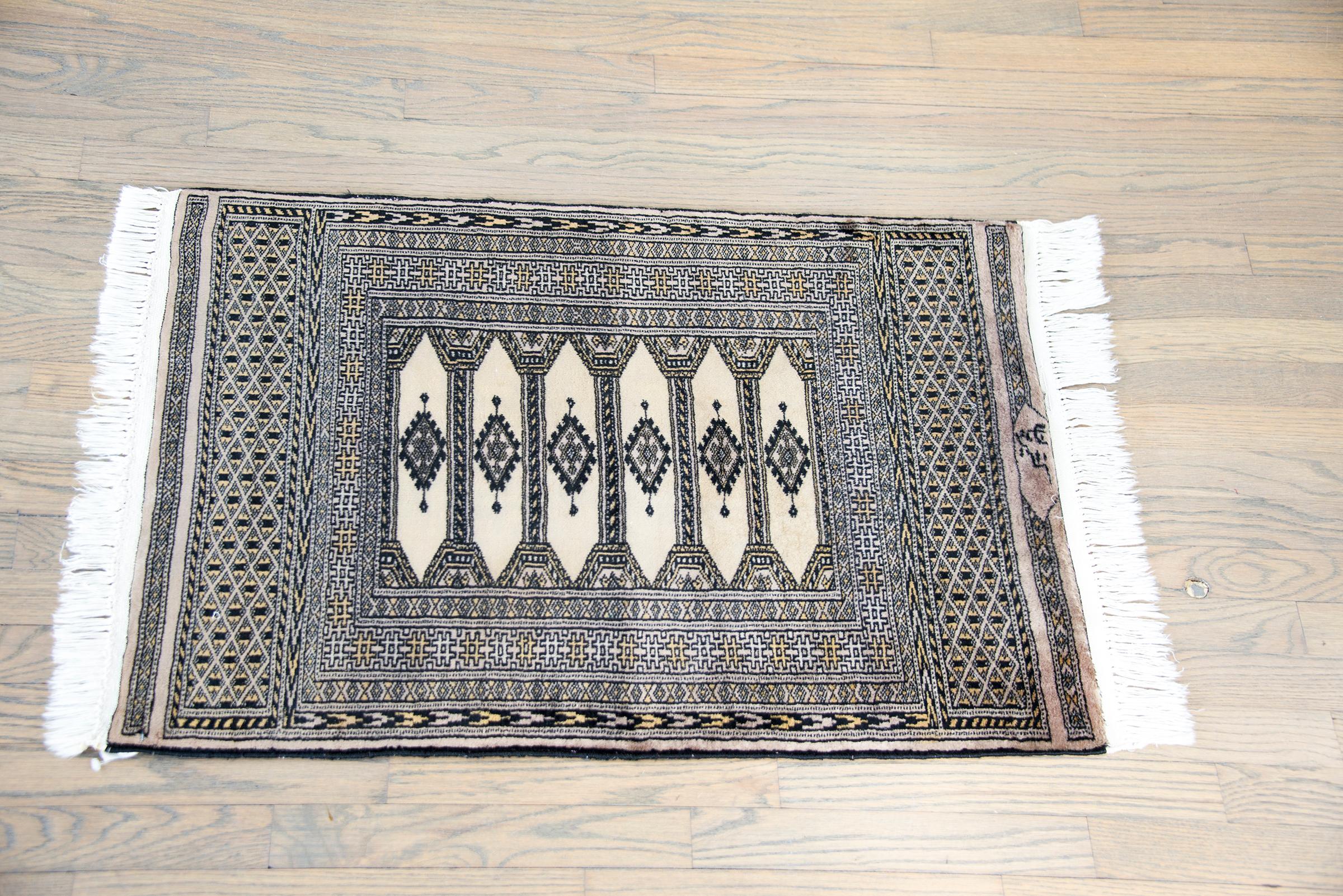 A vintage late 20th century Pakistani Bokhara rug with six large long central medallions surrounded by multiple thin and wide geometric patterned stripes, and with large grid patterned bands at the ends, and all woven in varying shades of pale