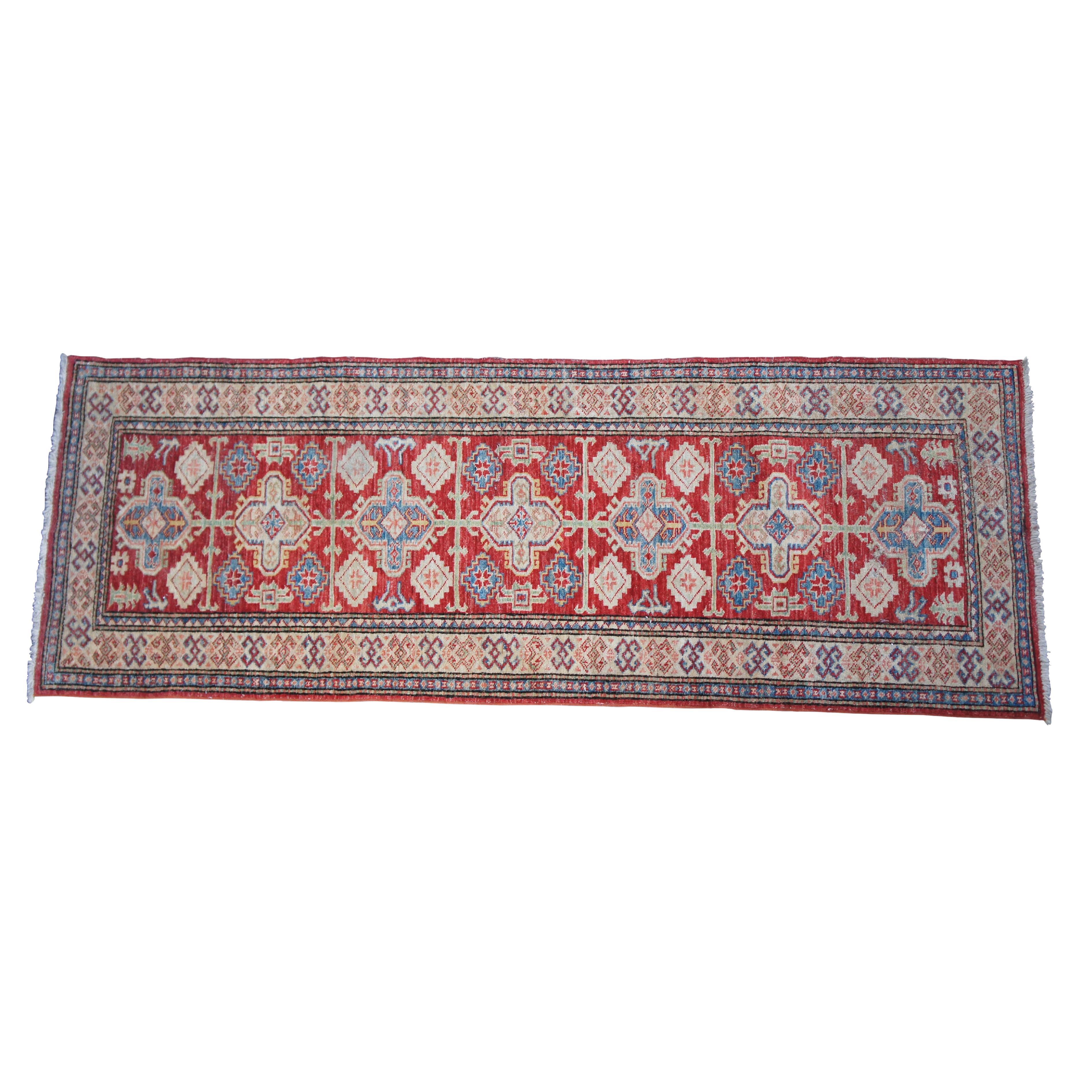 A colorful Persian Kazak rug runner.  Features a geometric design of blue, beige and green over a red foreground. Made in Pakistan.  

Kazak rugs are a type of Oriental rug that are known for their durability and unique knots. They are hand-knotted