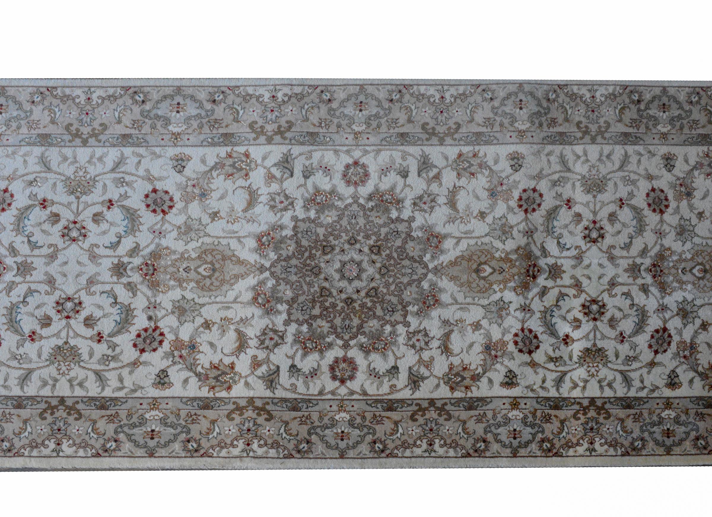 A beautiful vintage Pakistani runner woven with a Tabriz pattern containing several large medallions woven with scrolling vines and flowers woven in muted colors including brick red, rose, gray, steel blue, and gold, against a silver background, and
