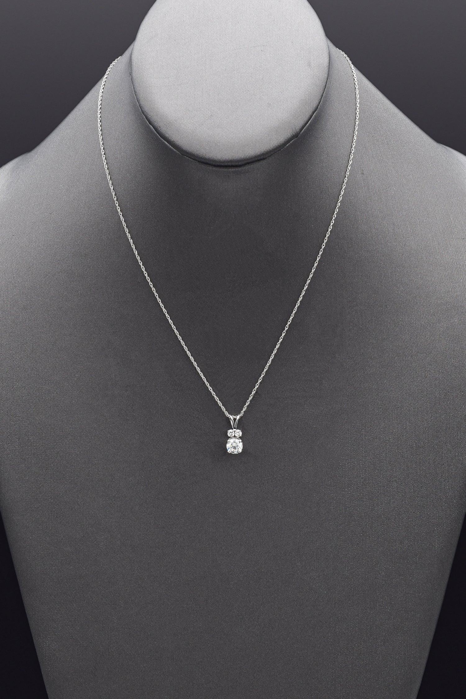 A stunning diamond pendant necklace. It features a primary round brilliant diamond. This diamond is beautifully flanked by two secondary round brilliant diamonds, adding balance and symmetry to the design. The setting is sleek and modern, showcasing