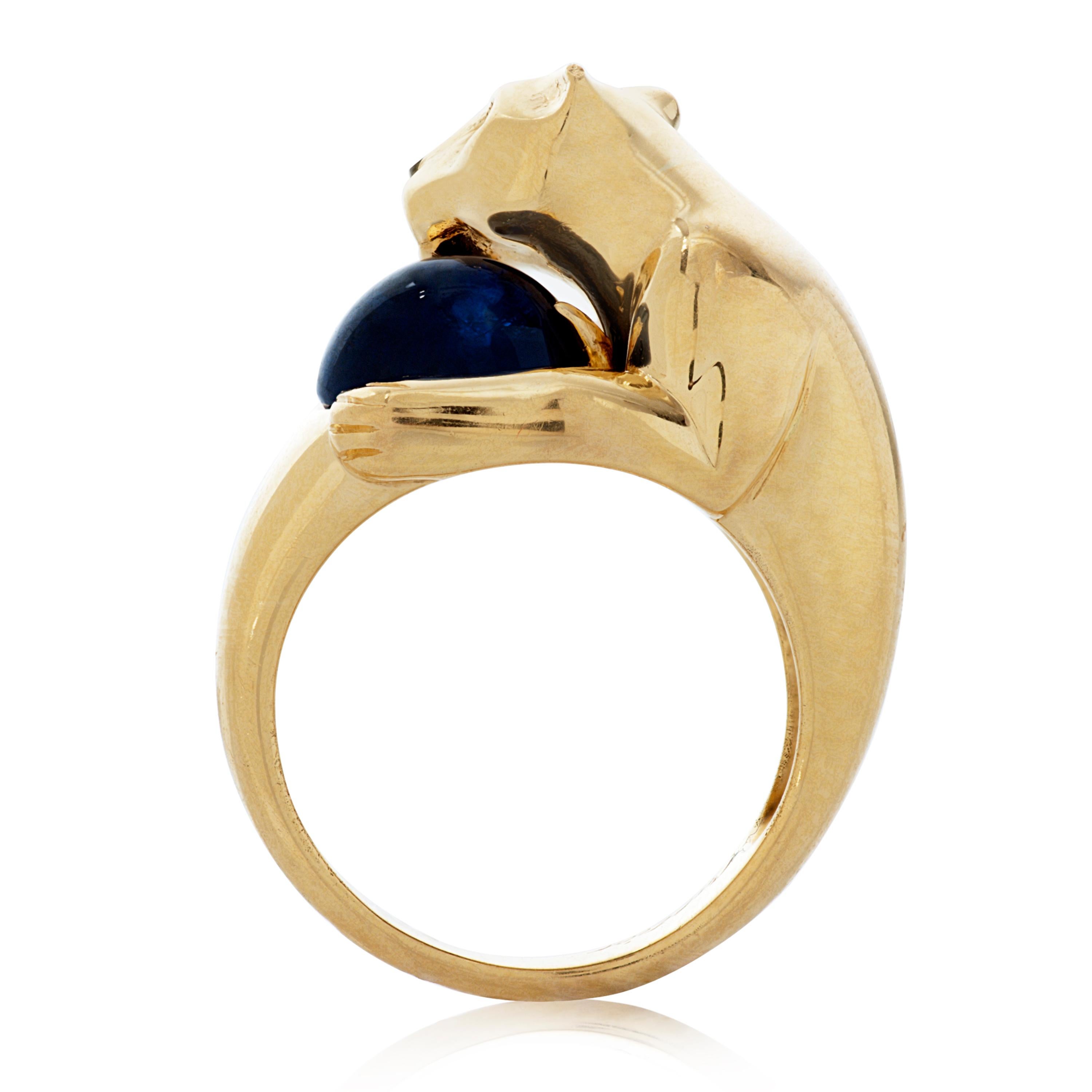 This vintage Panthere De Cartier ring features a panther holding an oval cabochon blue sapphire weighing approximately 4.40 carats.  The panther itself has two round emerald eyes and a carved onyx nose, set in 18k yellow gold.  Accompanied by