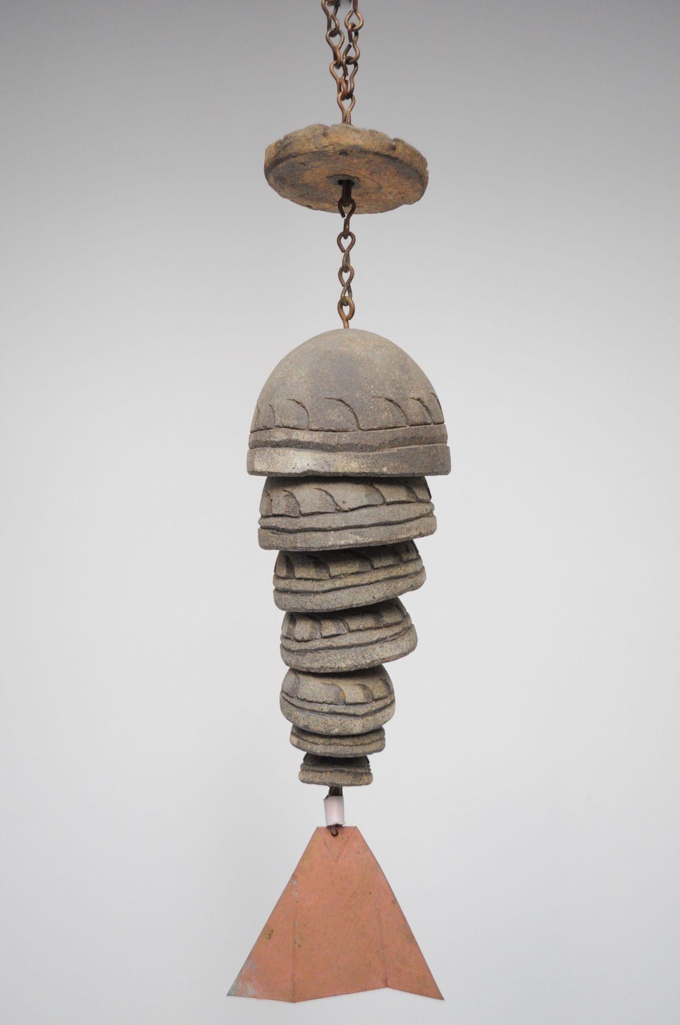 Fish-form wind chime/bell designed by architect, Paolo Soleri for Arconsanti (the city he designed and built in Arizona in 1970).
Composed of a chain suspending a clay disc above seven graduated/nesting cupped bells with hand-incised decorations and