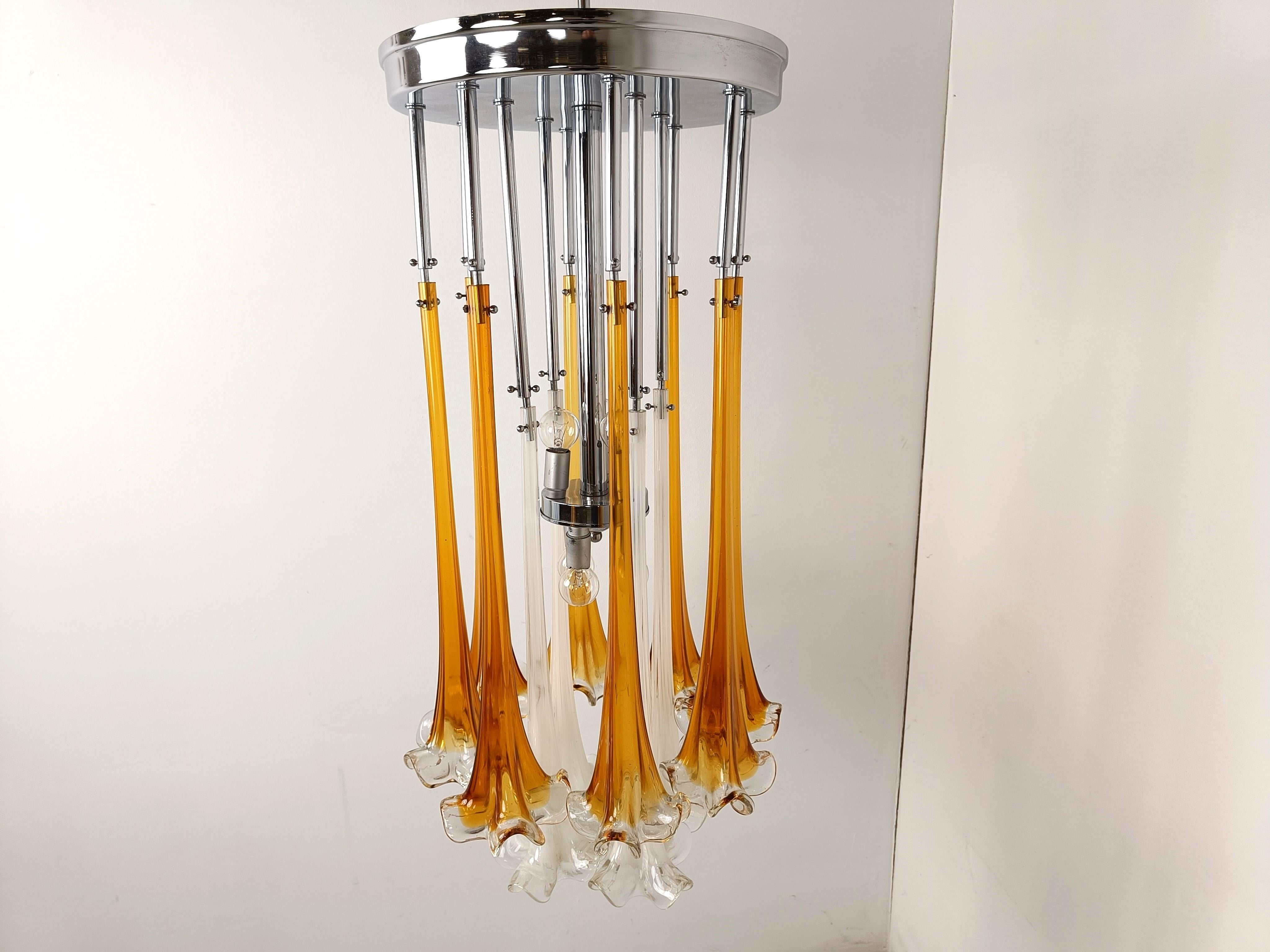 Striking murano glass chandelier by Paolo Venini.

The chandelier has a chrome frame with beautiful hand made murano glass flower shaped glasses.

To contrast the orange glass it also has two white glasses in the center.

Once lit, it really shows