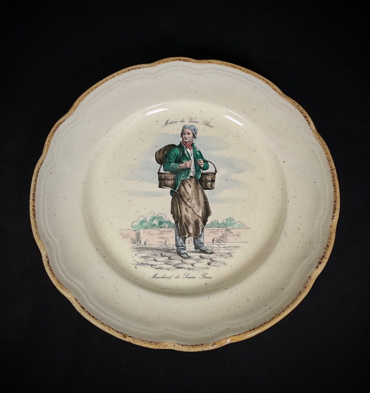 Beschreibung: Dieser entzückende dekorative Teller im Vintage-Stil fängt die Essenz des Pariser Charmes mit seiner komplizierten Darstellung eines traditionellen Eimerhändlers ein. Das Design steht auf einem gewellten Rand mit einem gesprenkelten