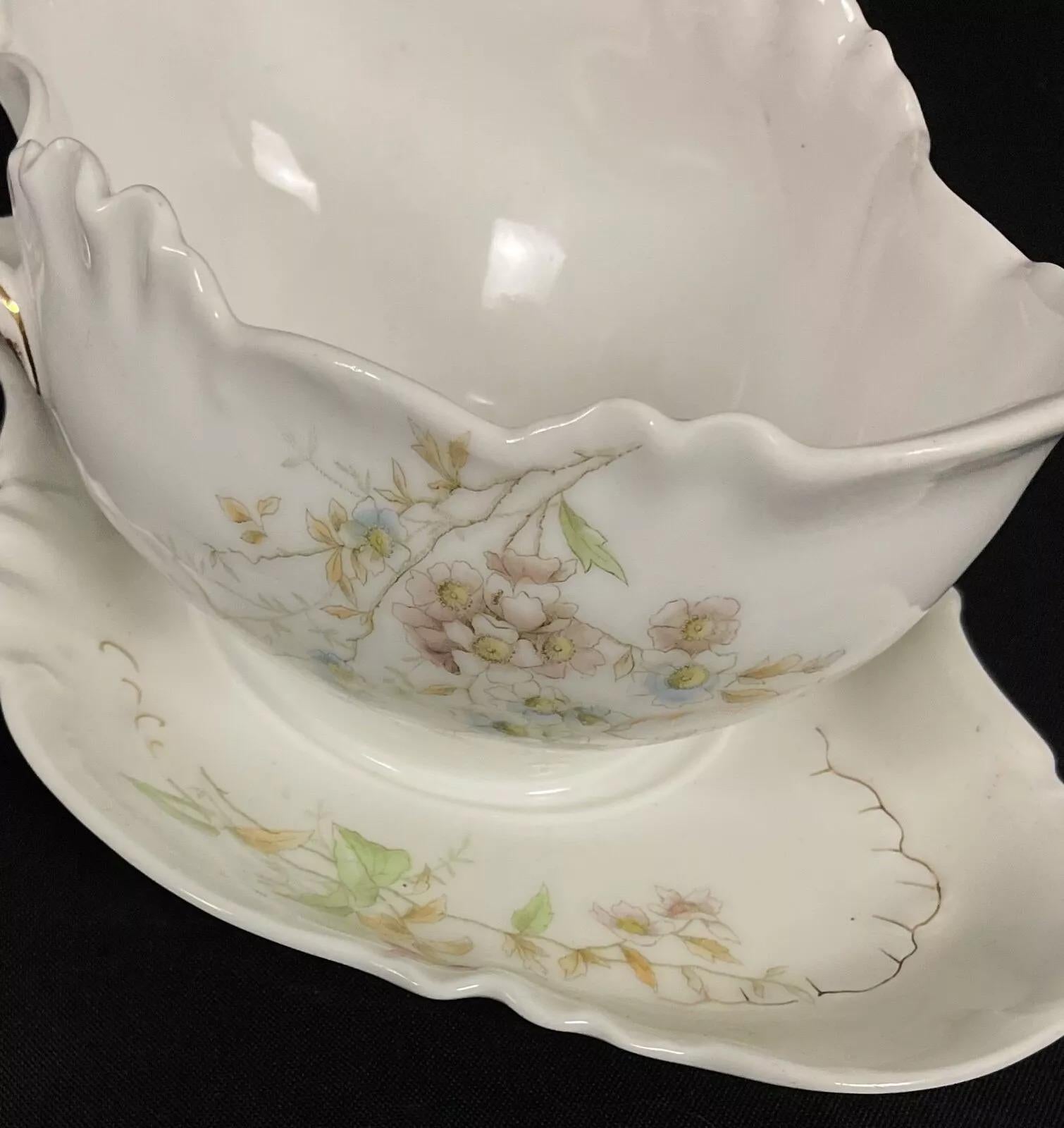 Diese antike Keramik-Sauciere aus dem 20. Jahrhundert, die von der berühmten Auguste Werner in Würzburg geschaffen wurde, ist ein zeitloses Stück funktioneller Kunst. Mit ihrem raffinierten weißen Sockel, der mit zarten Blumenmustern und goldenen