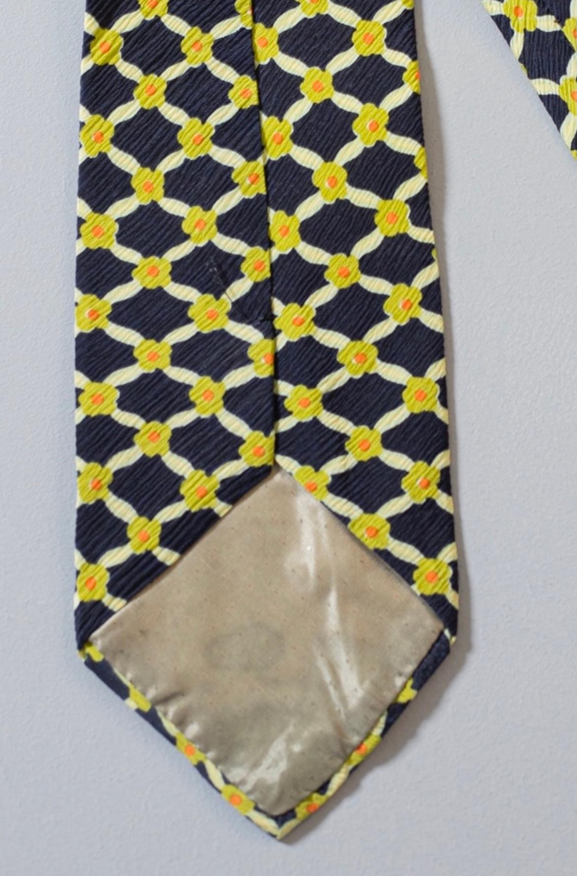 Cette cravate est d'une élégance intemporelle, conçue par Pascal, elle est réalisée en 100% soie. Décoré de petites fleurs jaunes sur un fond bleu, les fleurs sont jointes pour former de petits losanges. 
Idéal pour une belle soirée romantique aux