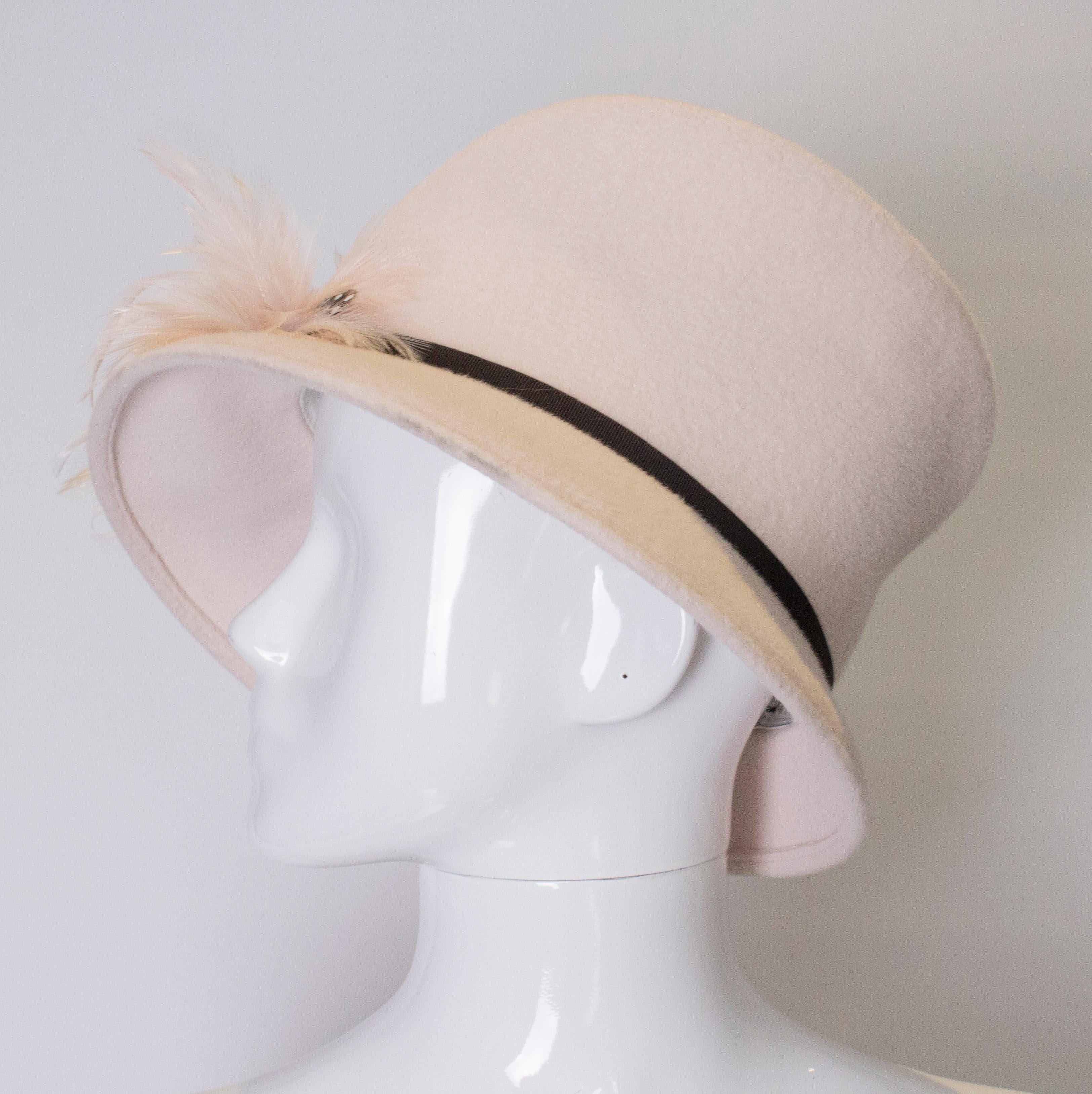 A chic and head turning hat by Emma B design. The has is in a soft pink colour with brown grossgrain ribbon and feather decoration. Inner circumference 25''.