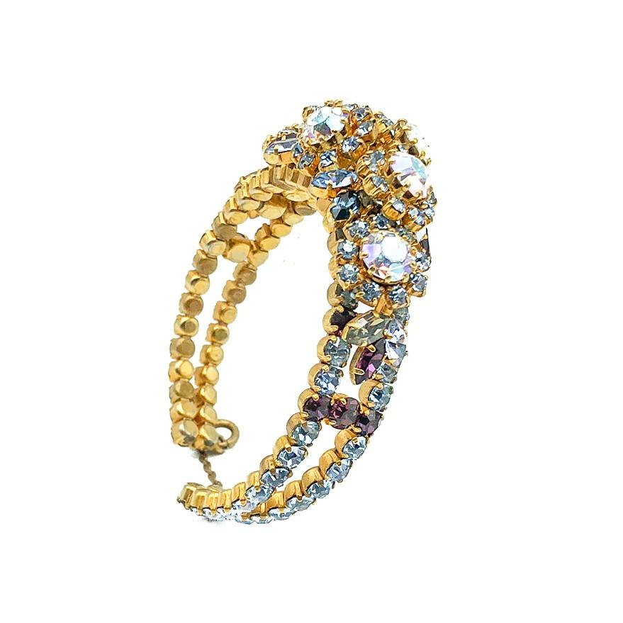 Un magnifique bracelet manchette vintage en strass pastel. Il est orné d'une multitude de cristaux autrichiens sertis en bleu, violet, rose et aurore boréale. Les pierres formant des fleurs sont montées sur un bracelet de manchette ouvert