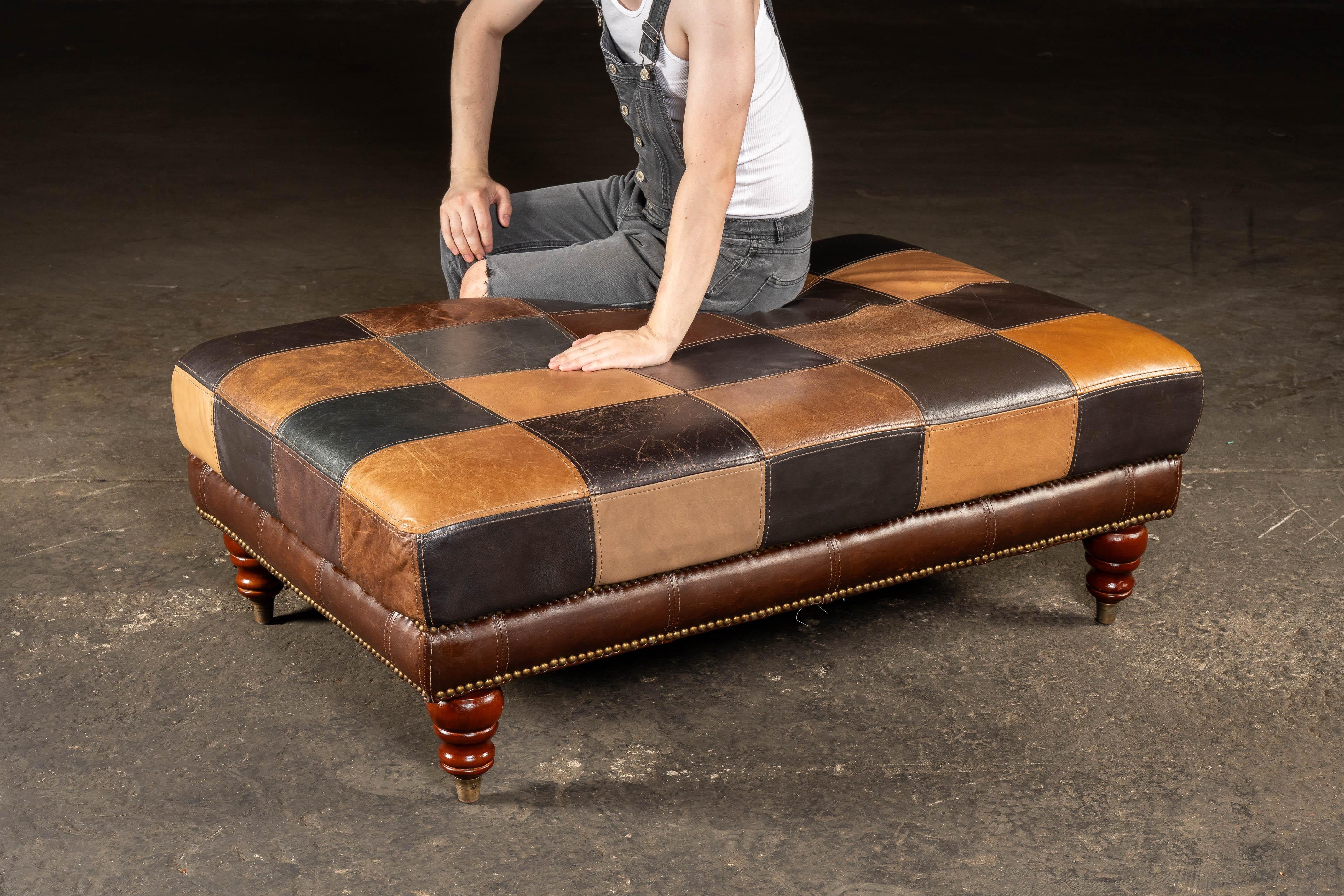 Kräftiger und funktioneller Leder-Ottoman aus einem Patchwork aus reichhaltigen, vollnarbigen Häuten in warmen Farbtönen, der auf gedrechselten Holzfüßen mit Messingkappen ruht.

Dieser großzügig bemessene Ottoman misst 49