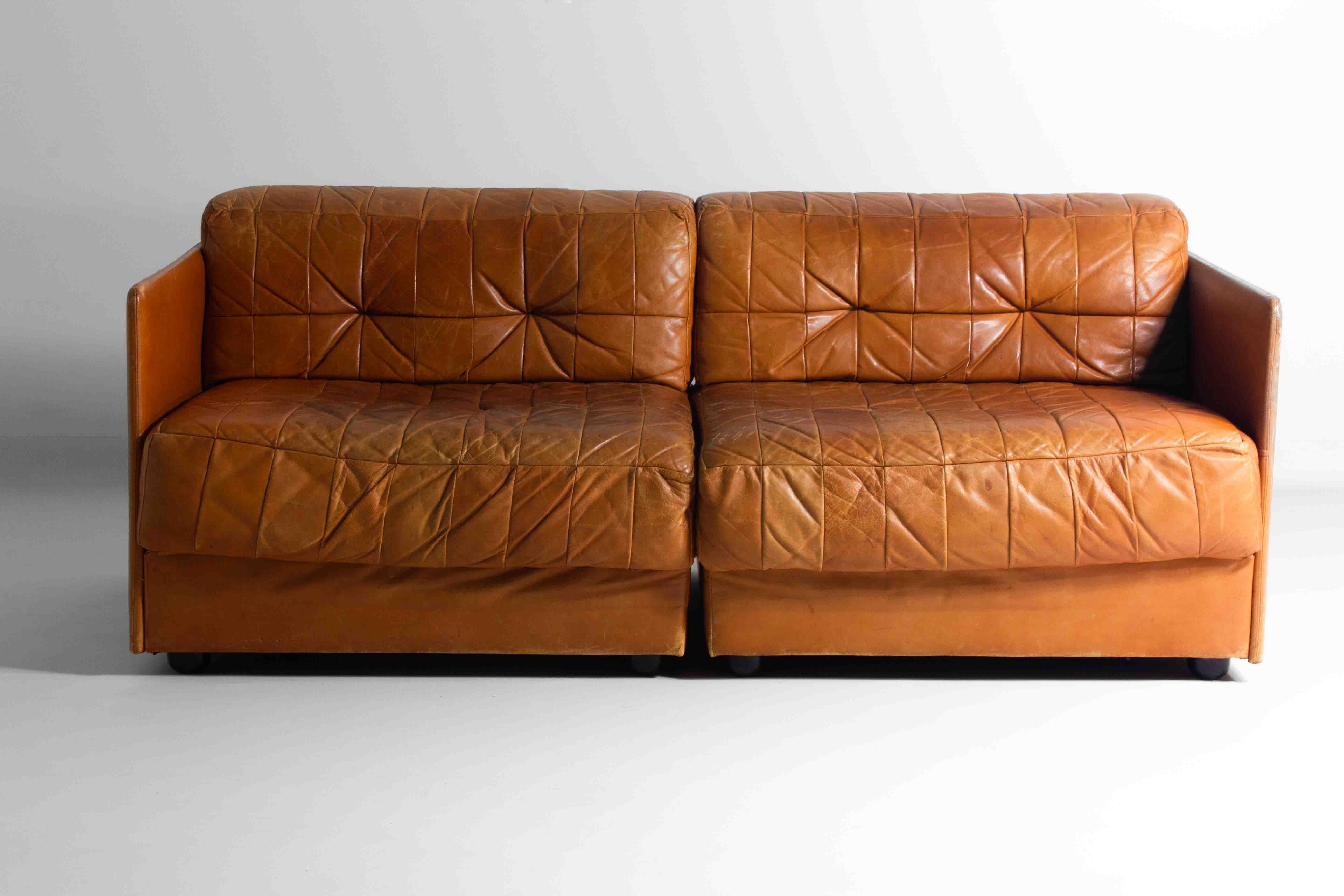 his sofa has a real vintage charm with its patchwork leather design. The caramel brown color gives it a warm, inviting look, and the way the patches are put together adds a unique character. It’s got that comfy, inviting vibe that makes you want to