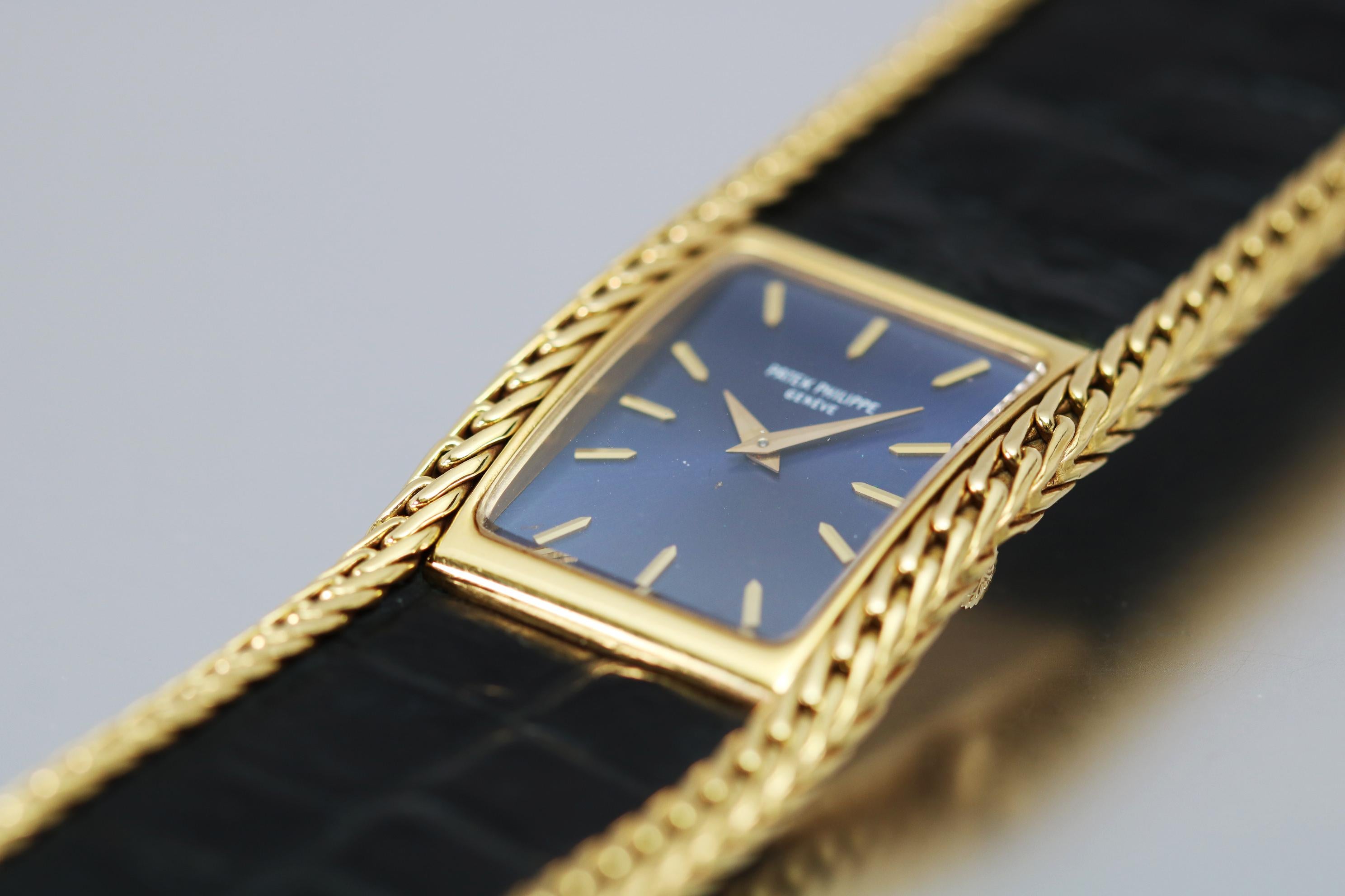 Vintage Patek Philippe Lady's Wristwatch Ref 4241. This rectangular blue gilt dial is in an 18k yellow gold rectangular case with an integrated bracelet made of leather and flanked by gold braided link. It is run with a manual wind cal. 16-250