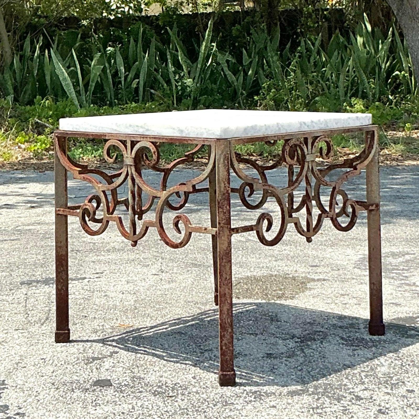 Cette table d'appoint vintage allie sans effort l'élégance rustique à un design intemporel. La base en fer forgé à la main présente des volutes complexes et une patine magnifiquement altérée, évoquant le charme du vieux monde et le travail