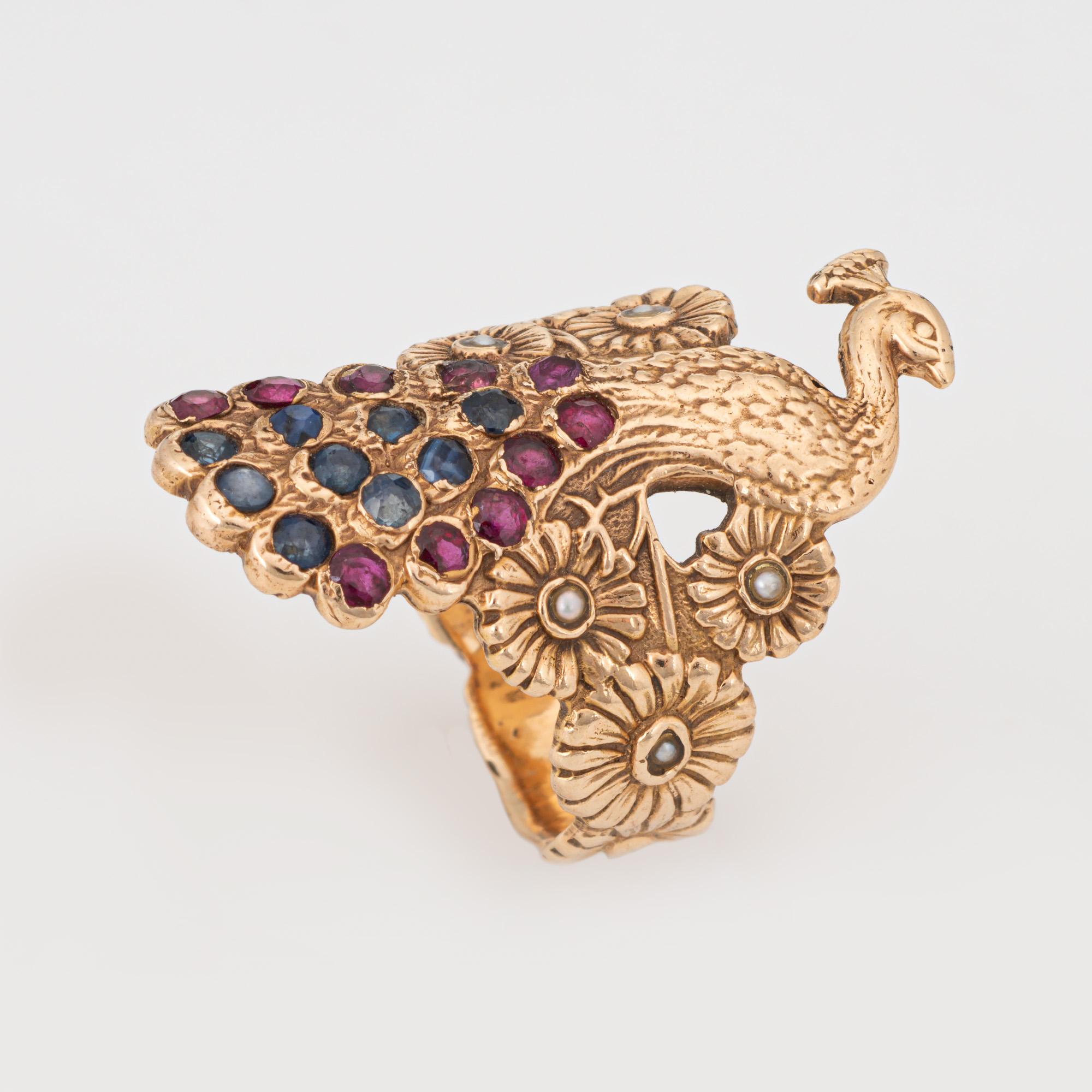Stylish vintage Peacock ring crafted in 14 karat yellow gold. 

Rubies and sapphires measure 1.5mm each, accented with 1mm seed pearls. The gemstones are in good condition with light wear evident.   

The elaborate Peacock features sapphires and