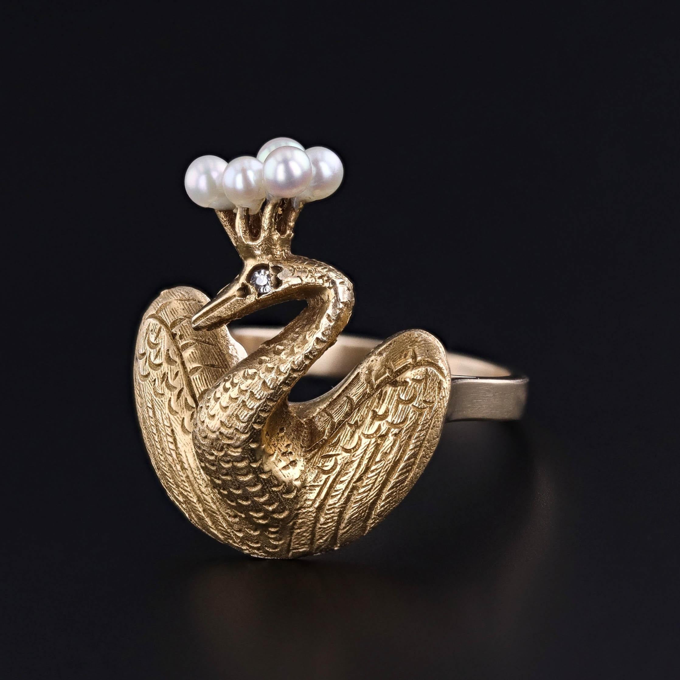 Ein königlicher Ausdruck von Kunstfertigkeit und Verwandlung: Dieser einzigartige Ring zeigt einen majestätischen Pfau aus 14-karätigem Gold, der stolz mit einer zarten Perlenkrone und einem Diamantauge geschmückt ist. Ursprünglich eine