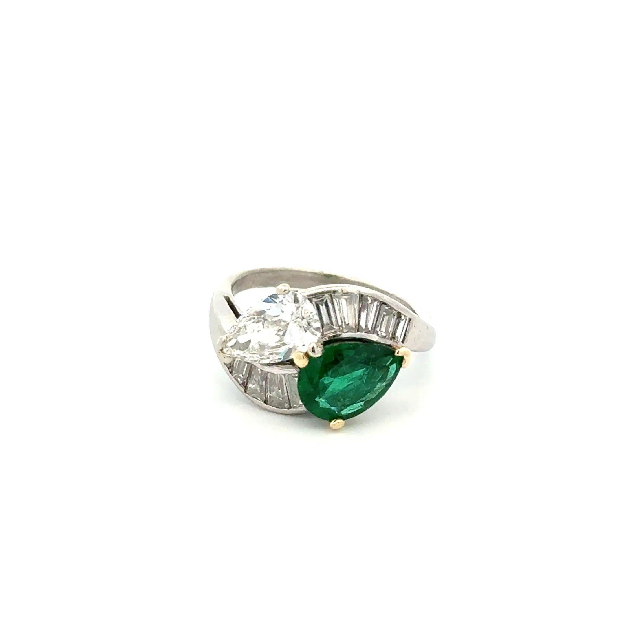 Simply Beautiful! Finely detailed, Vintage 'Toi et Moi' Cross Over Bypass Ring. Securely Hand set with a 1.05 Carat Pear Diamond, 1.40 Carat Emerald and .75tcw Baguette Diamonds. Hand crafted in Platinum and 18K Gold. Ring size 6, we offer ring