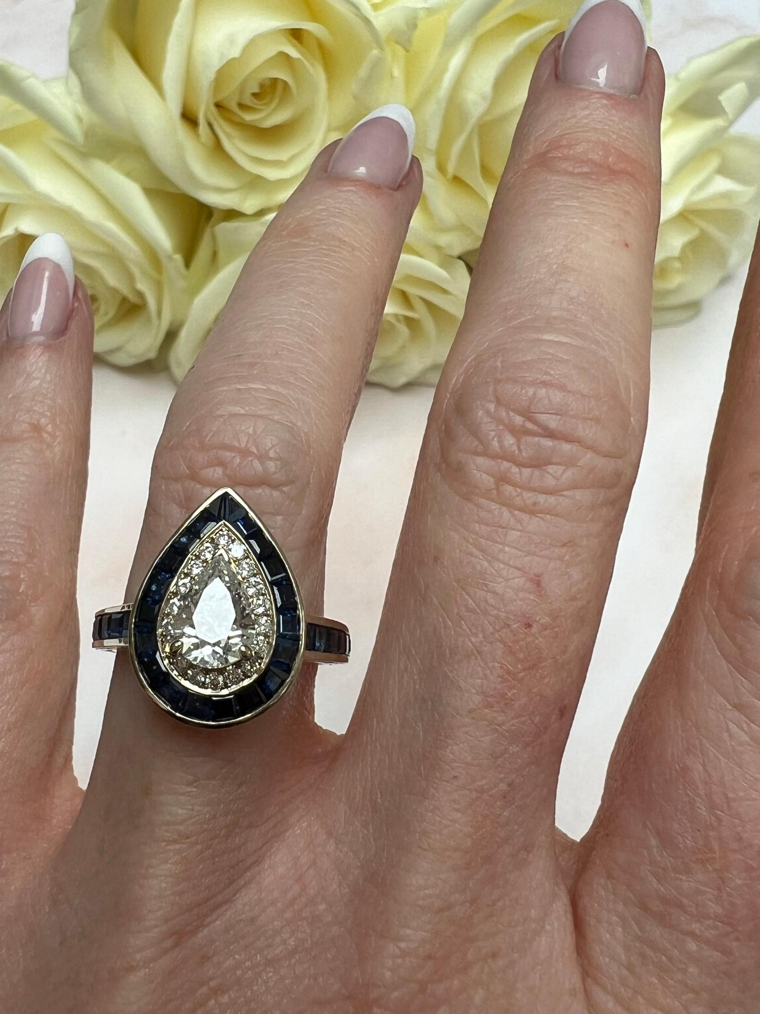 Vintage pear shaped diamond and sapphire ring. This stunning ring centres with a 1ct pear diamond with a halo of brilliant cut diamonds (0.18cts) and then incredible calibre cut sapphires, set in white gold. Size 5.5/K.5