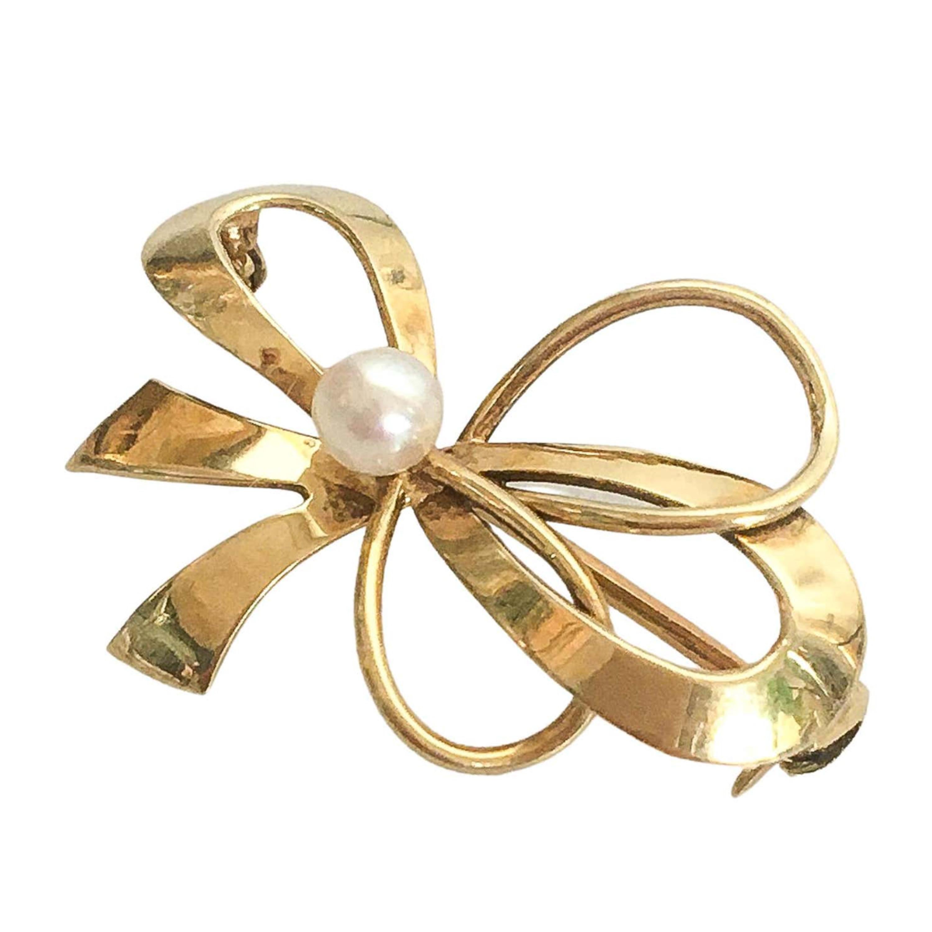 A classic vintage bow brooch crafted in 14 karat gold. The brooch is set with a clear round cultured pearl in the center. A timeless intricately designed and crafted ribbon bow. The brooch is secured with a roll-over safety catch. 

The lovely