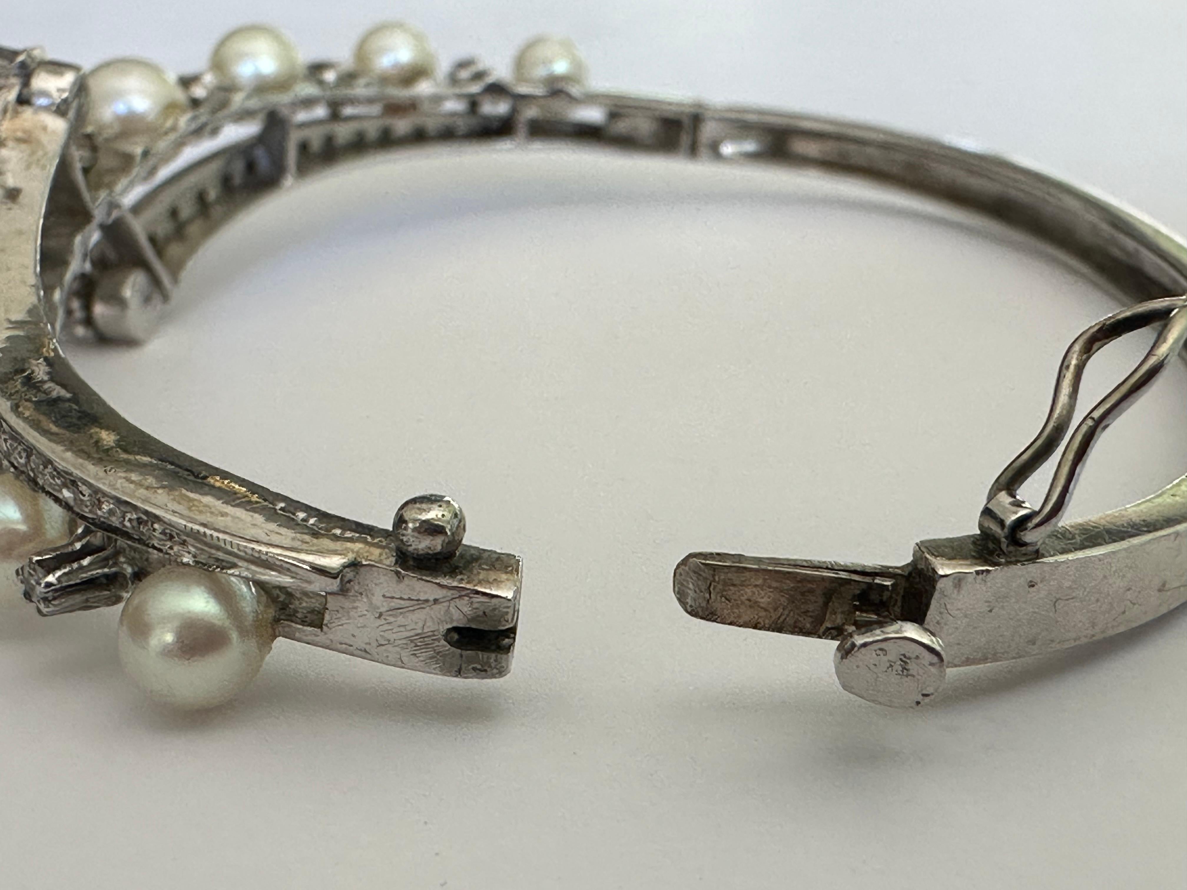 Dieses Vintage-Armband besteht aus neun weißen Perlen, die mit Diamanten im Einzelschliff von insgesamt ca. 0,25 Karat in einem klassischen Bypass-Design verziert sind. Gefertigt aus 10 Karat Weißgold. 


