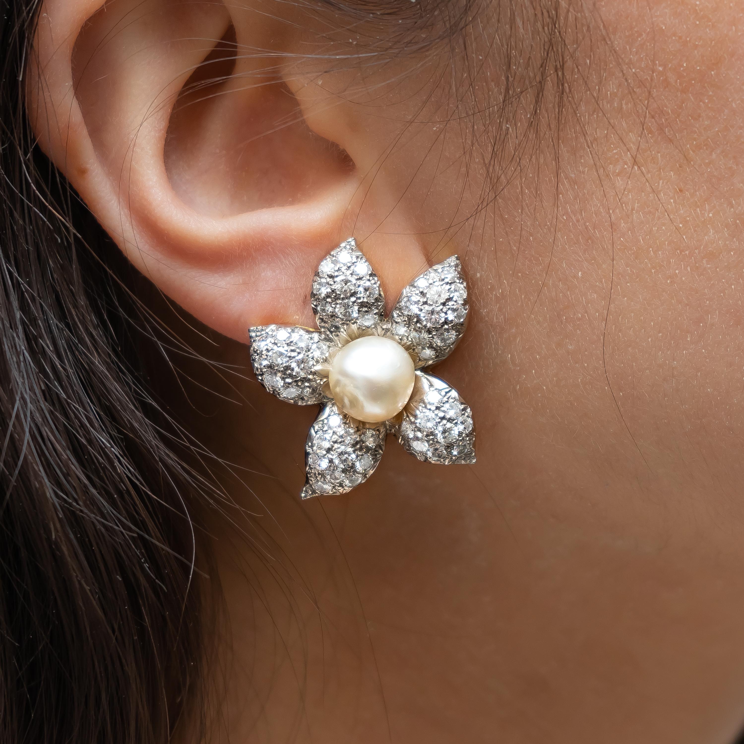 A pair of vintage diamond and natural pearl flower earrings, mounted in platinum on gold, with pavé set petals. The approximate total diamond weight is 11.00ct, the pearls measure approximately 10mm. Circa 1950.
