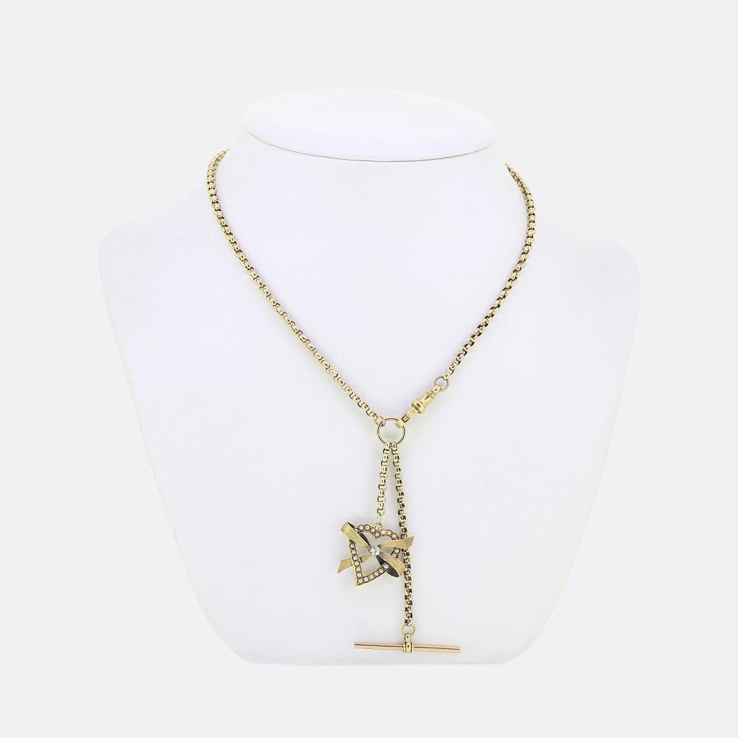 This is a vintage 9ct yellow gold belcher chain charm necklace. The necklace plays host to a duo of freely hanging motifs. Firstly, an open love heart pendant is framed by an array of natural seed pearls with a single round faceted diamond at the